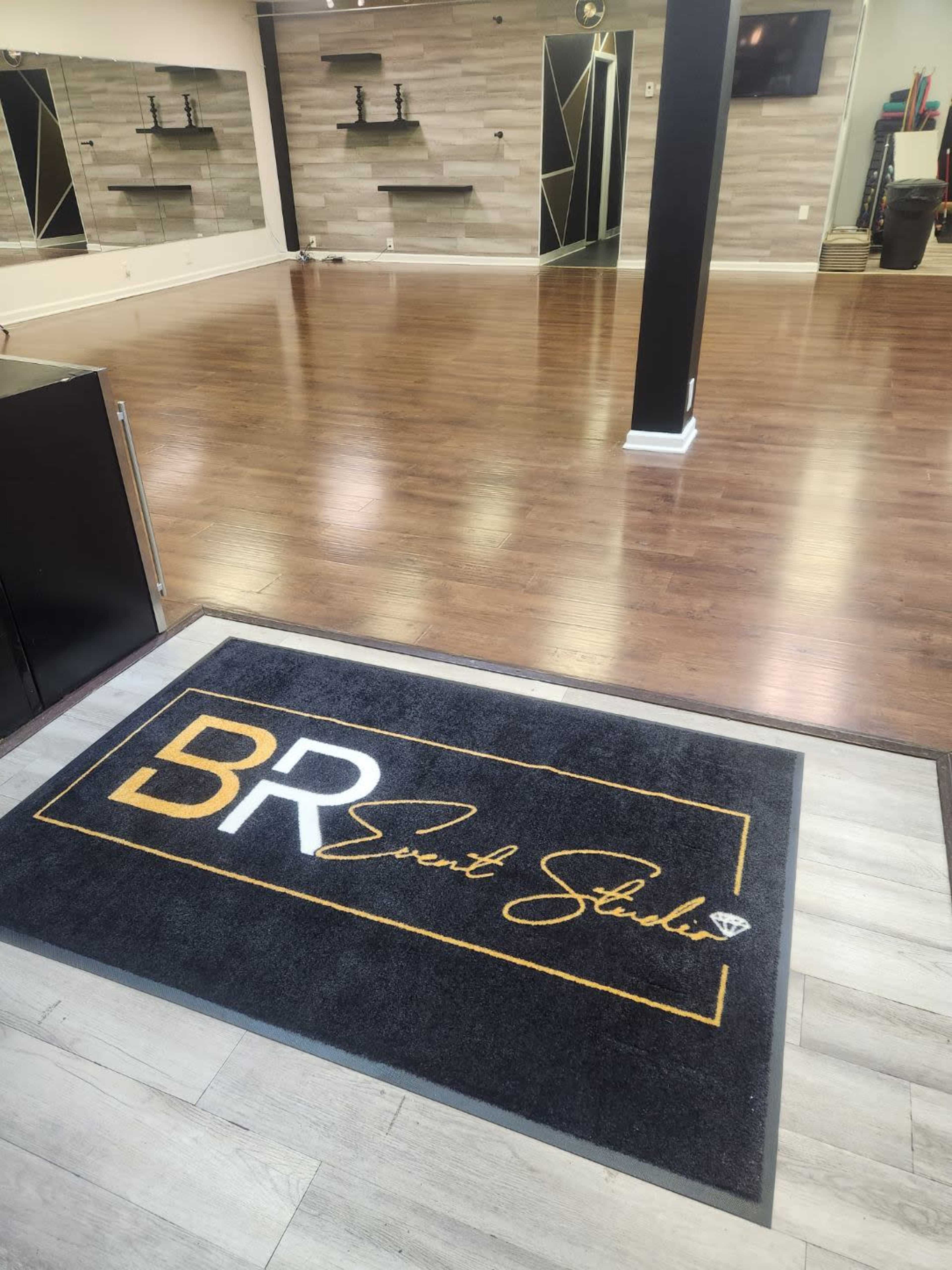 The interior of a studio featuring wooden flooring, a large mirror on the wall, and a welcome mat with "BR Dance Studio" prominently displayed.