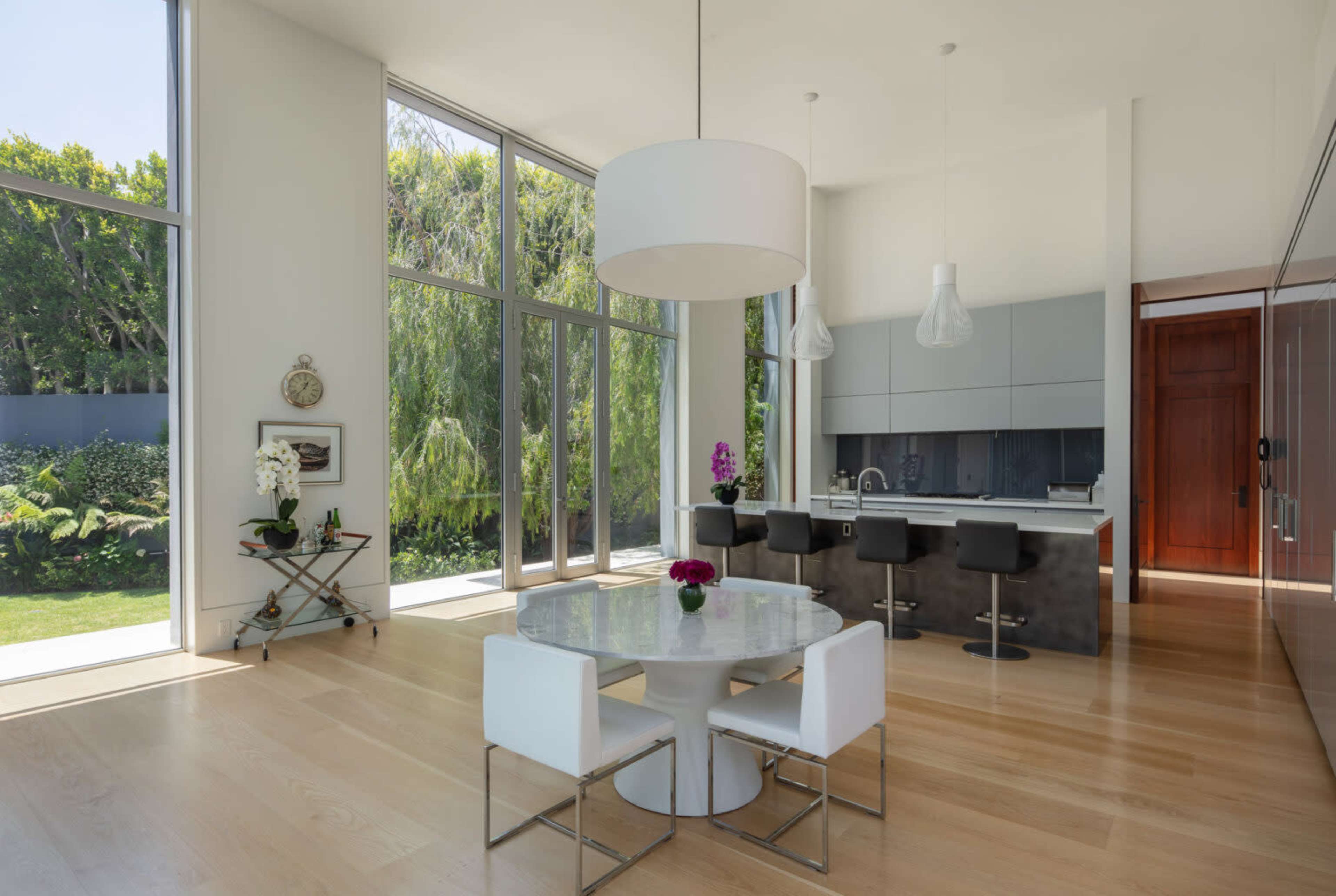 A modern kitchen and dining area with large windows, a round table, and sleek bar stools.