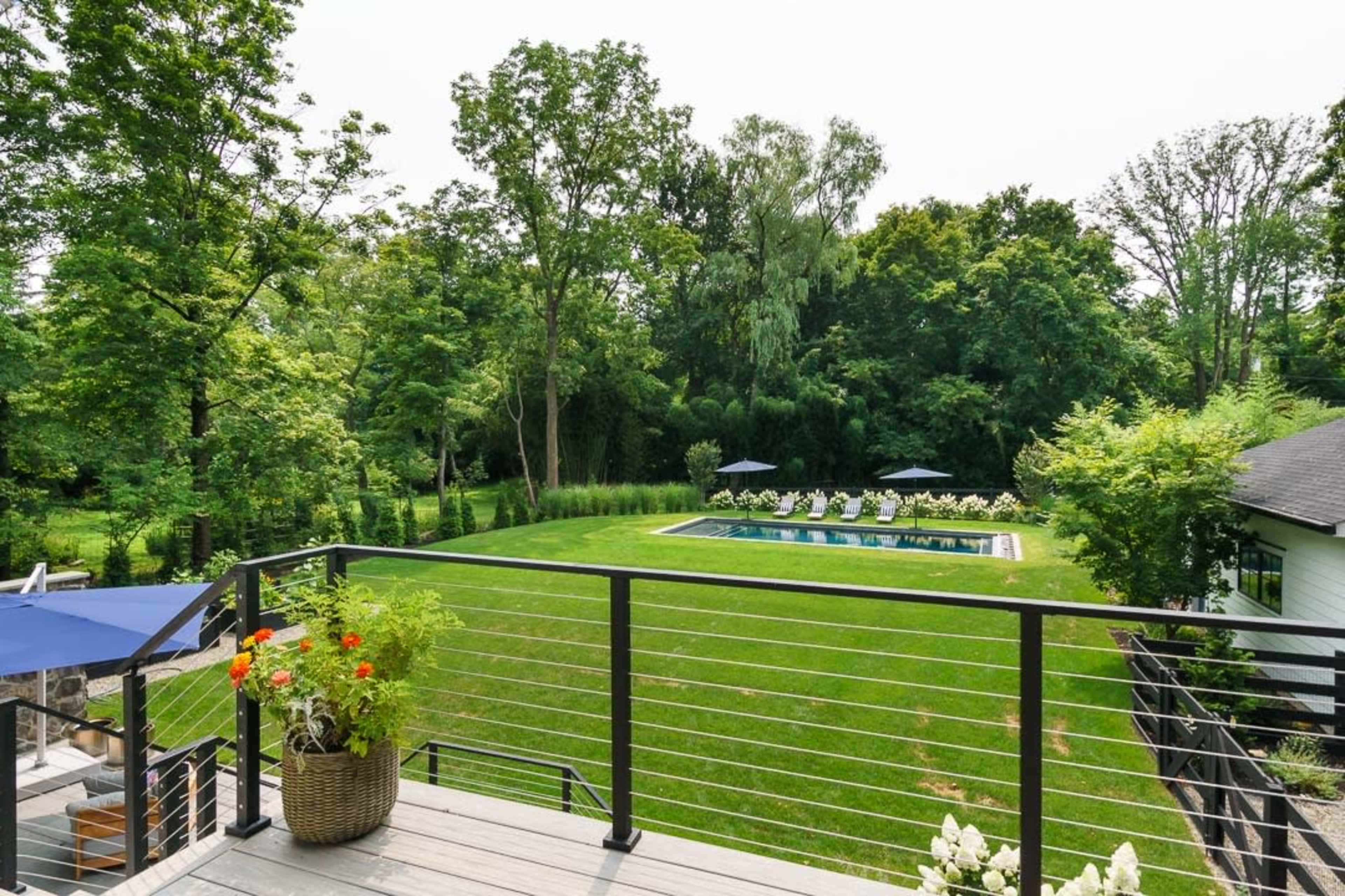 A deck overlooks a grassy area with a swimming pool surrounded by lounge chairs and trees.