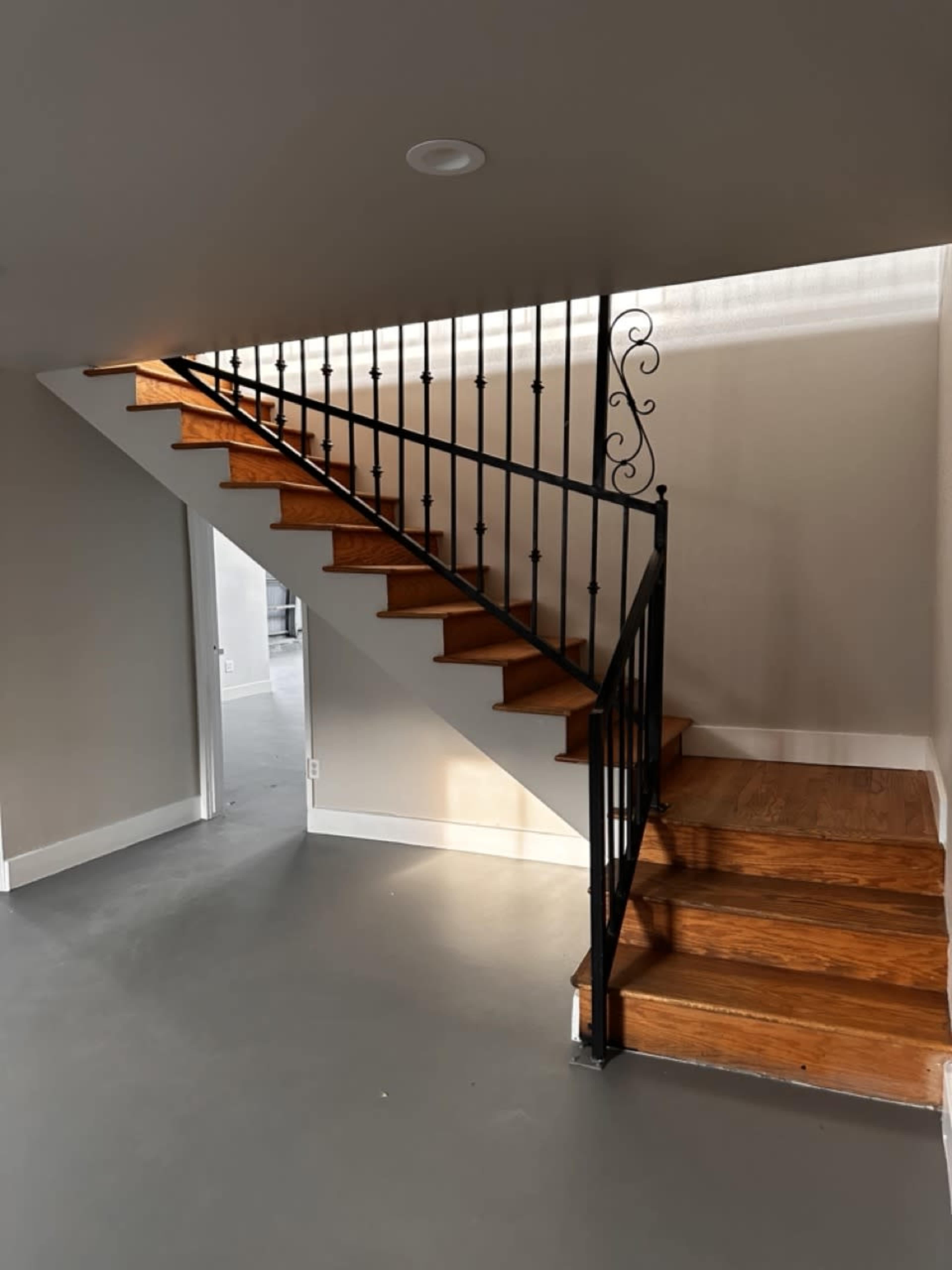 A wooden staircase with a black metal railing leads to an upper level in a minimalist room.