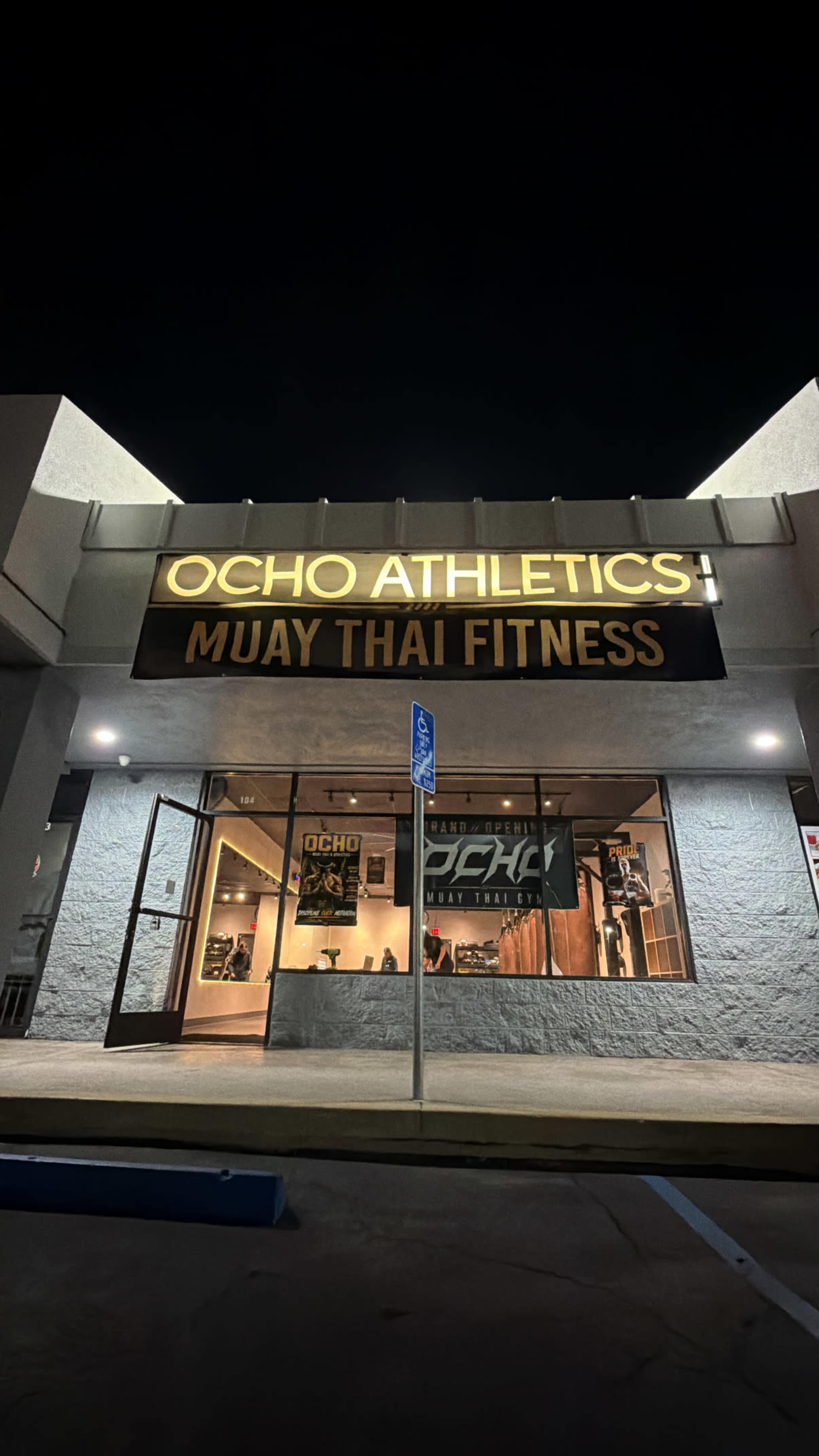 The image shows the exterior of a gym named Ocho Athletics, specializing in Muay Thai fitness, illuminated at night.