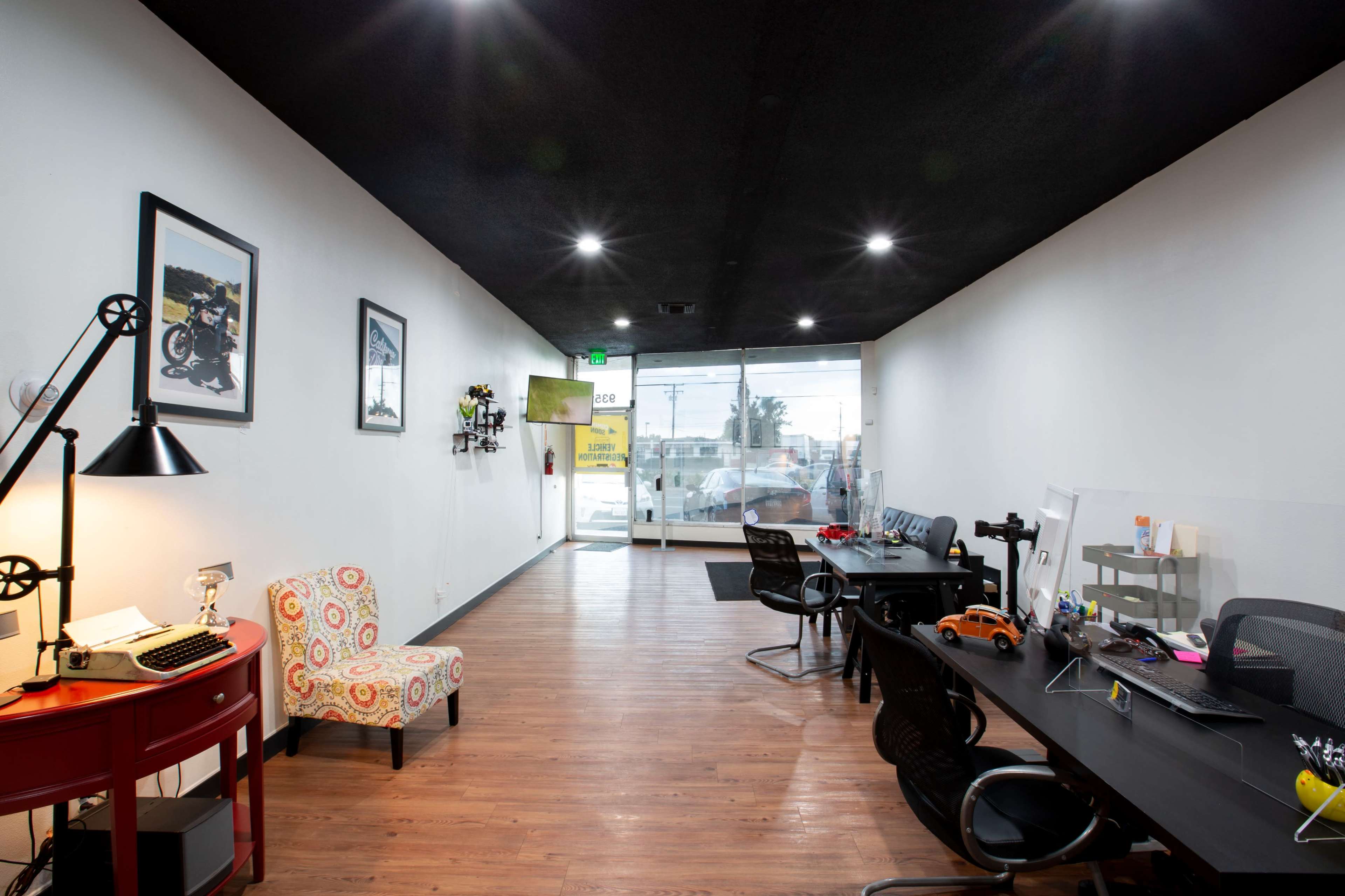 The image shows a modern office space with a reception area, workstations, and large windows allowing natural light to enter.