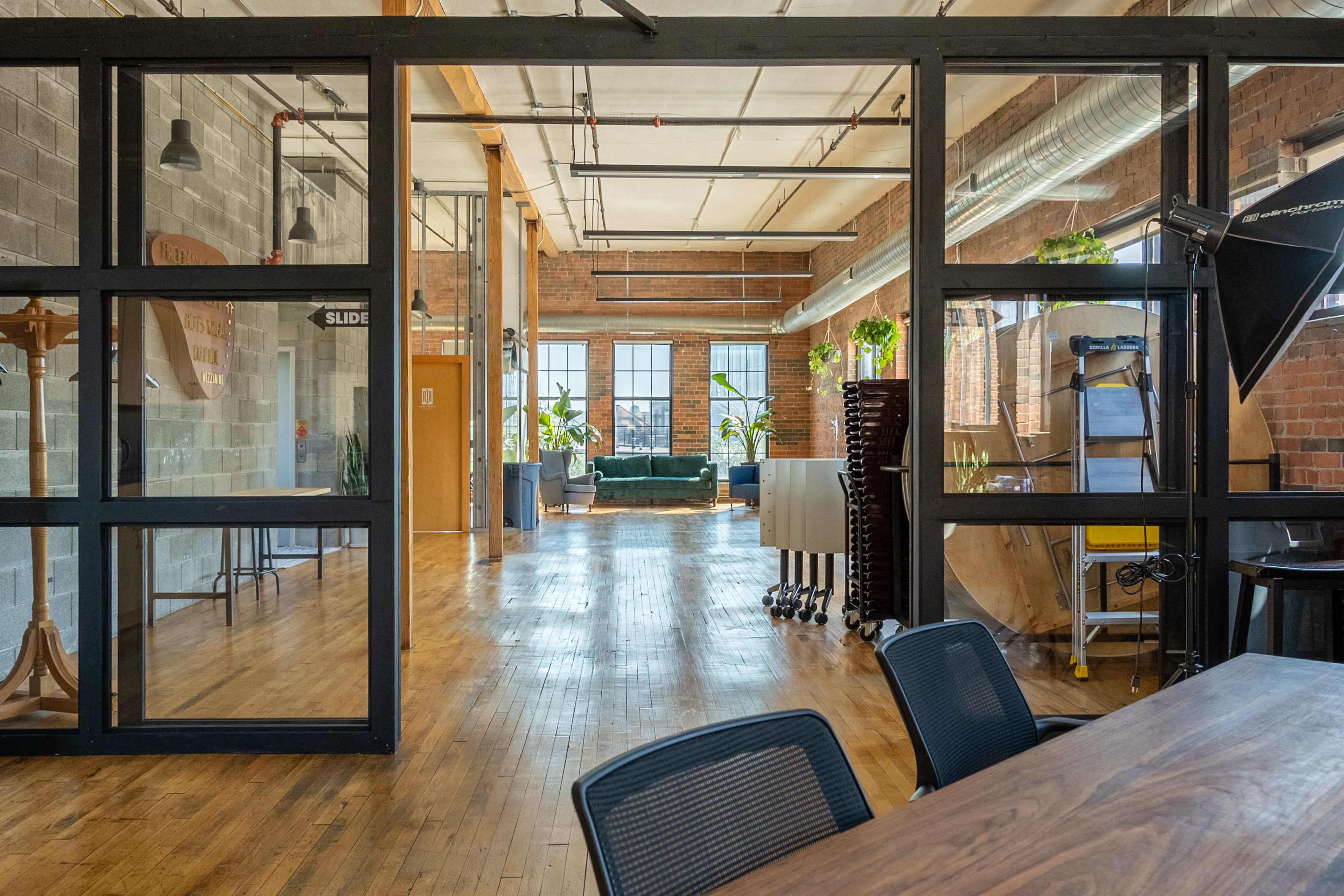 A spacious, modern office interior with large windows, wooden floors, and various workspaces separated by glass walls.