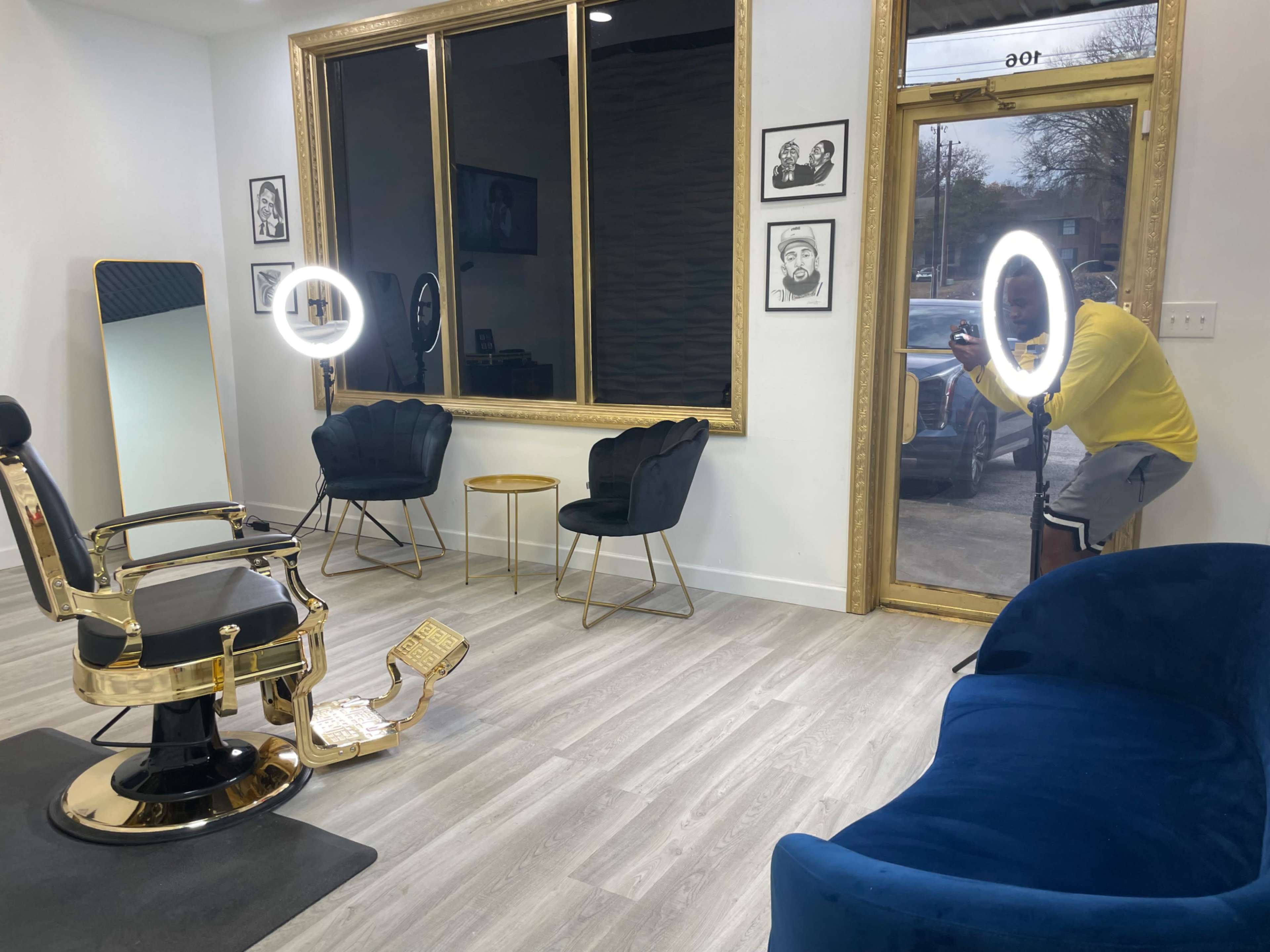 A modern barbershop interior with a gold-framed mirror, a barber chair, and a person taking a photo by the entrance.
