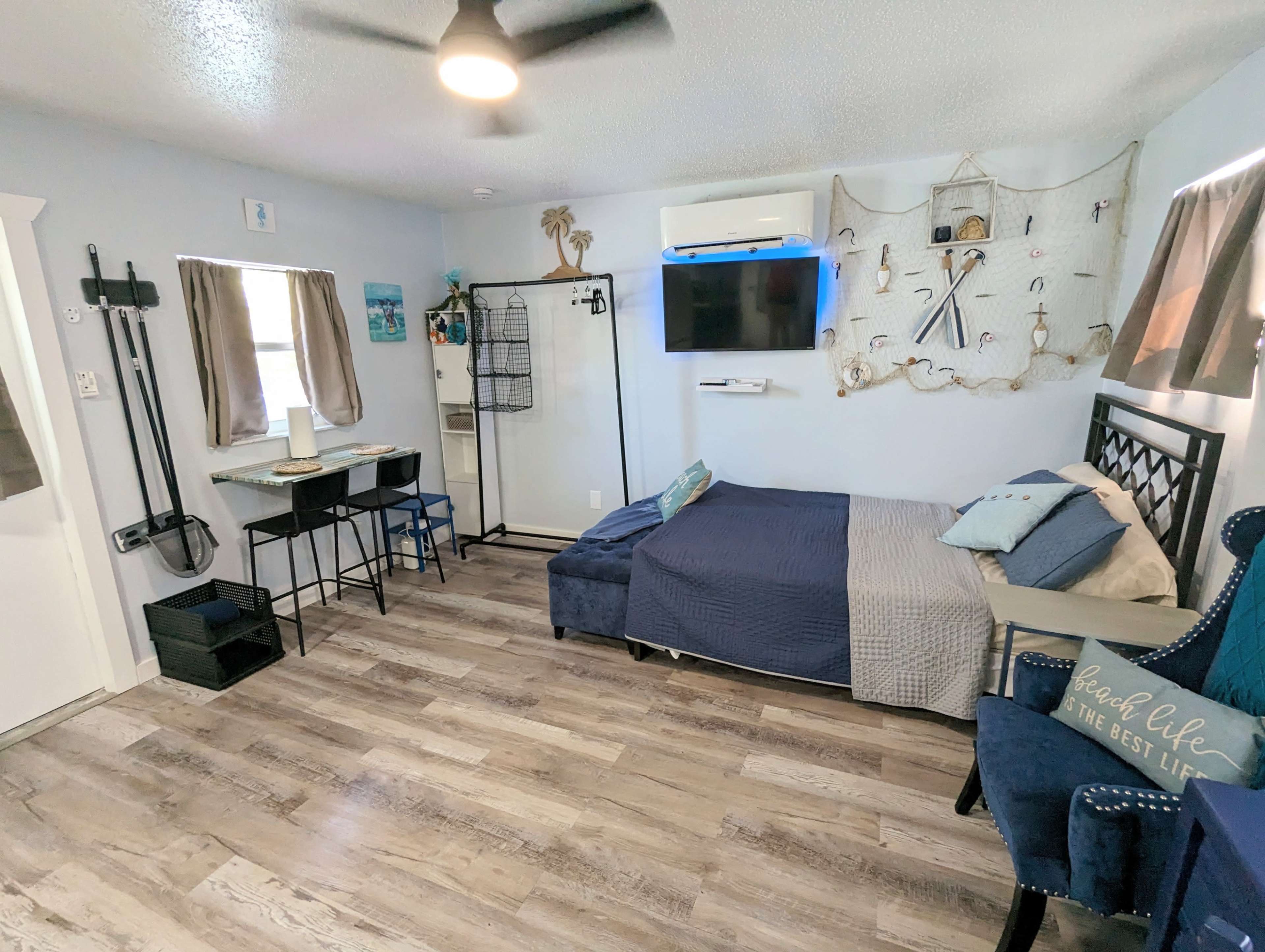 A cozy bedroom with a bed, a small desk and chairs, a wall-mounted TV, and beach-themed decor.