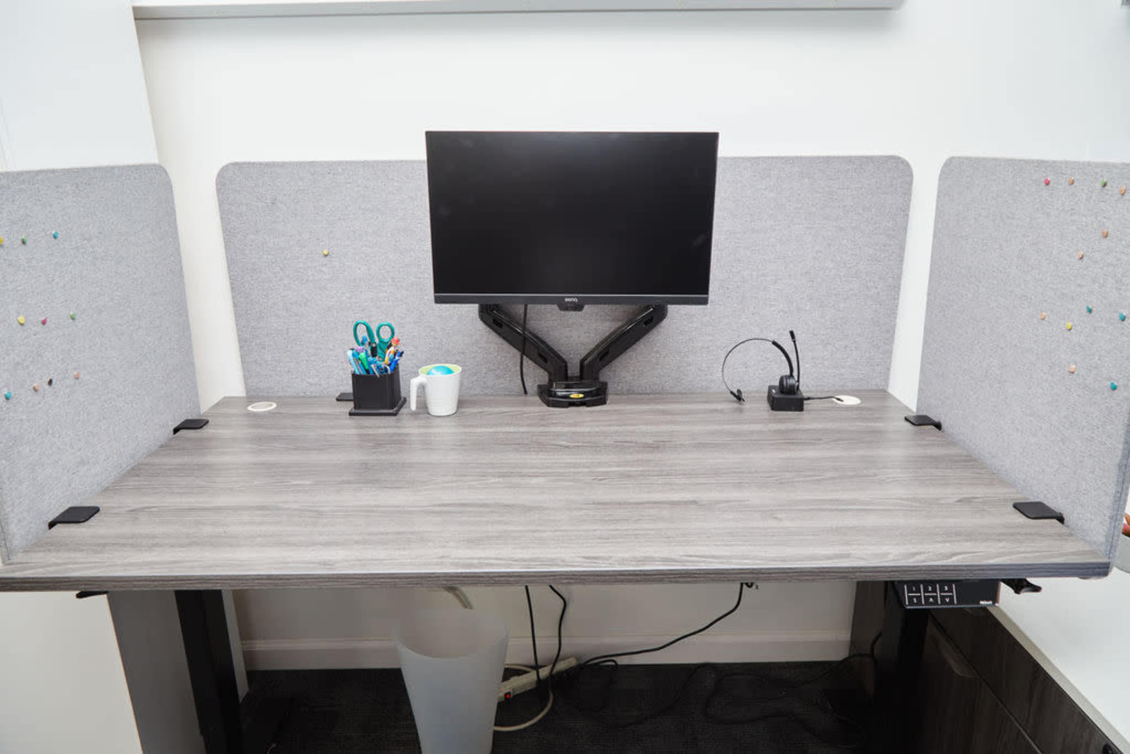 A modern desk setup features a monitor, stationery items, a headset, and acoustic panels on either side.
