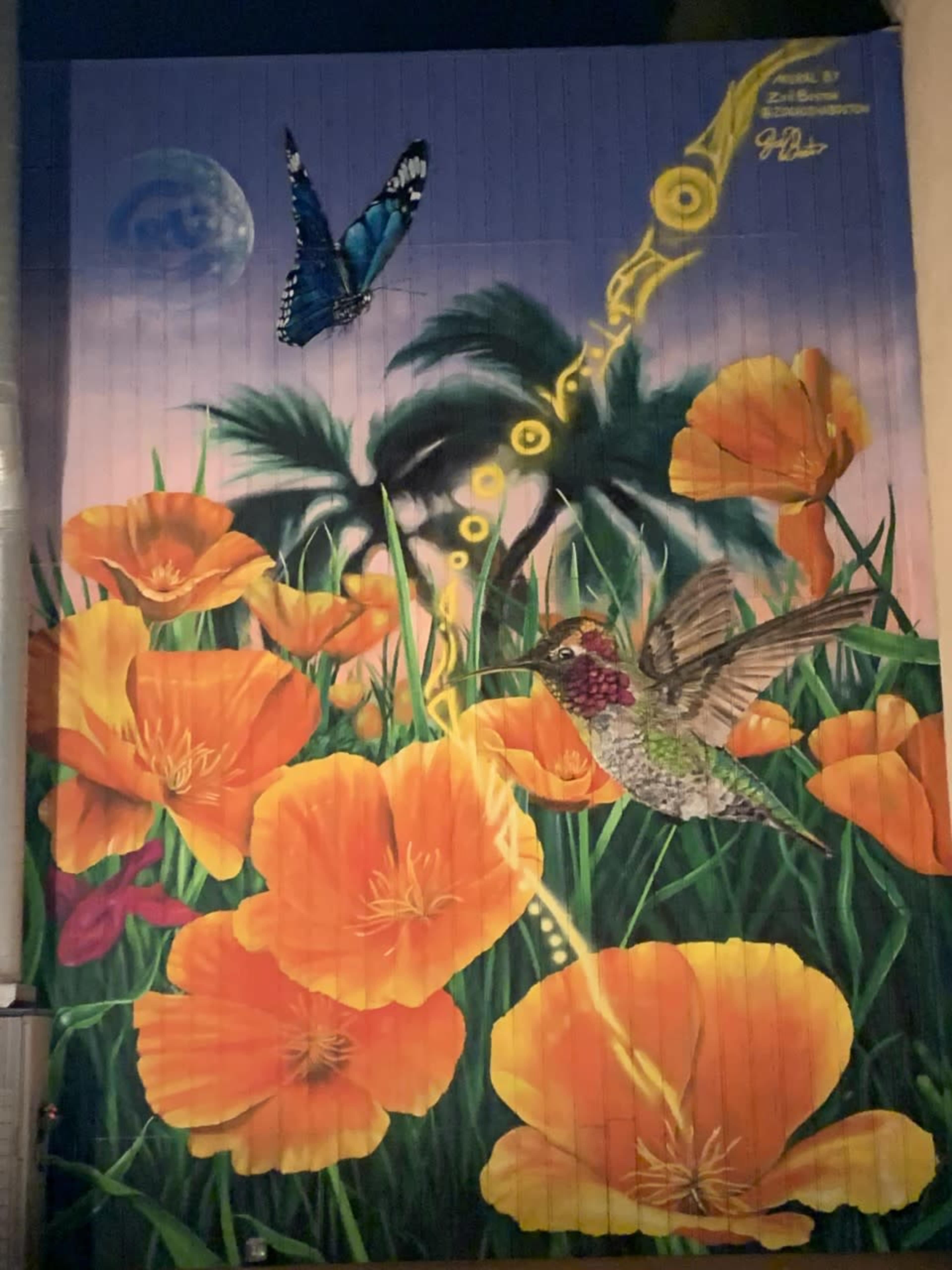 The mural depicts a butterfly and a hummingbird flying among vibrant orange poppies and tropical foliage against a purple sky.