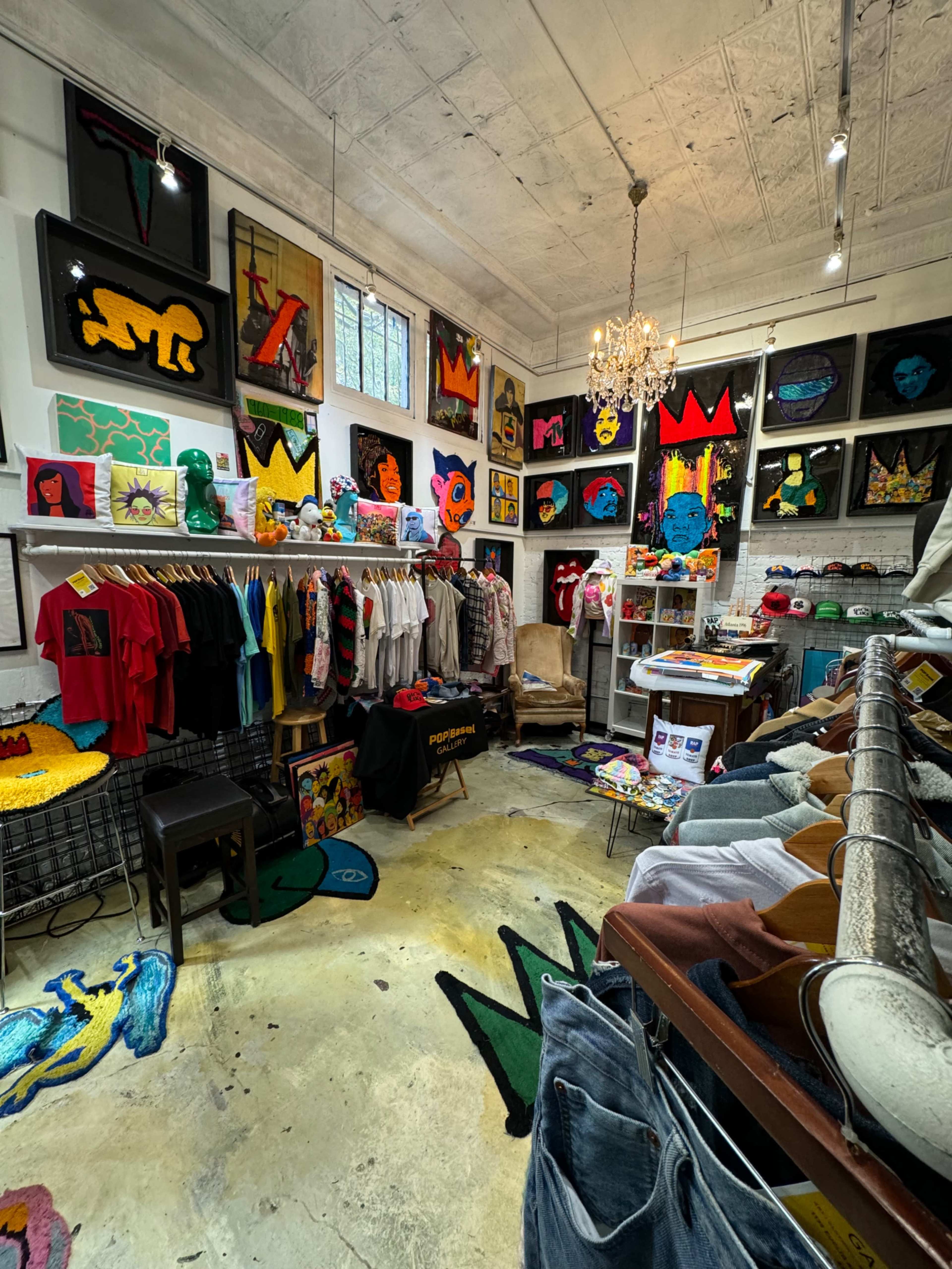 The image shows a colorful vintage clothing store with items displayed on racks, walls adorned with art, and a chandelier hanging from the ceiling.