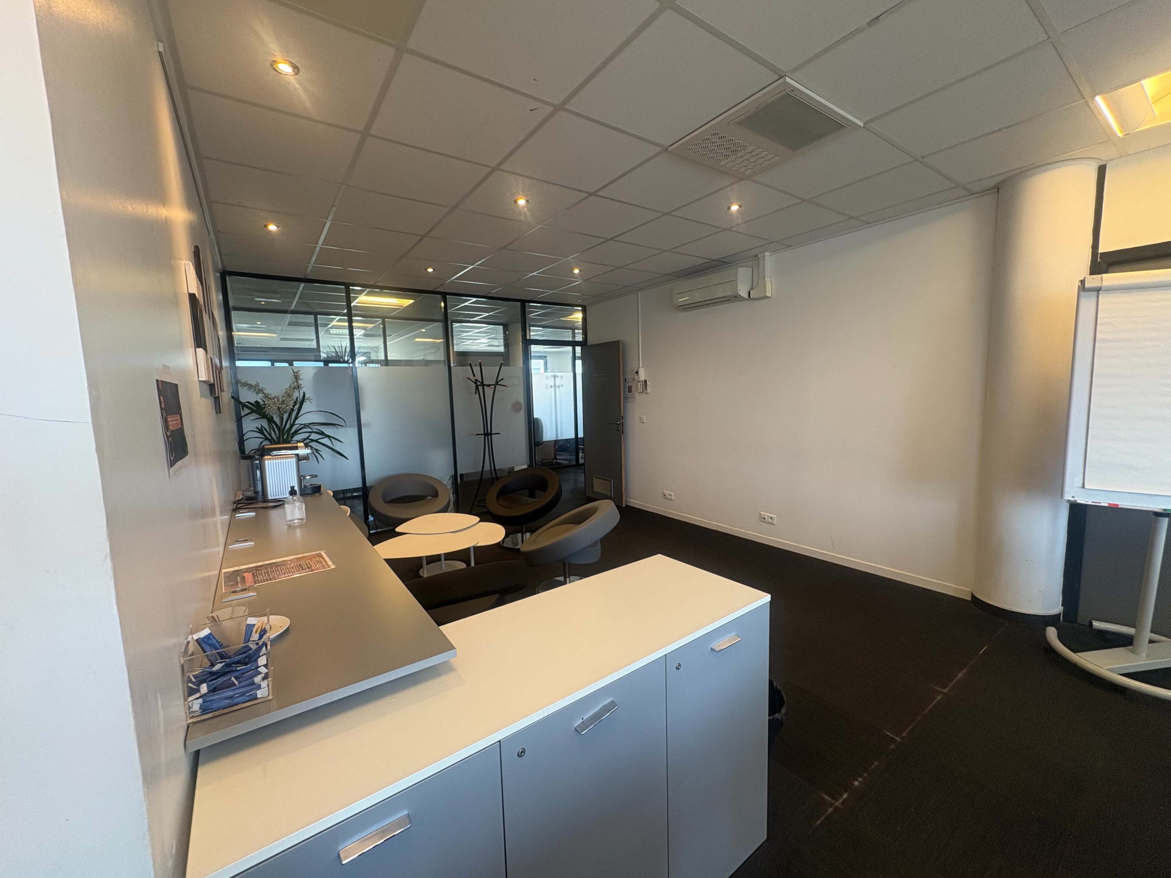 The image shows a modern office reception area with a countertop, several chairs, and partitions separating different workspaces.