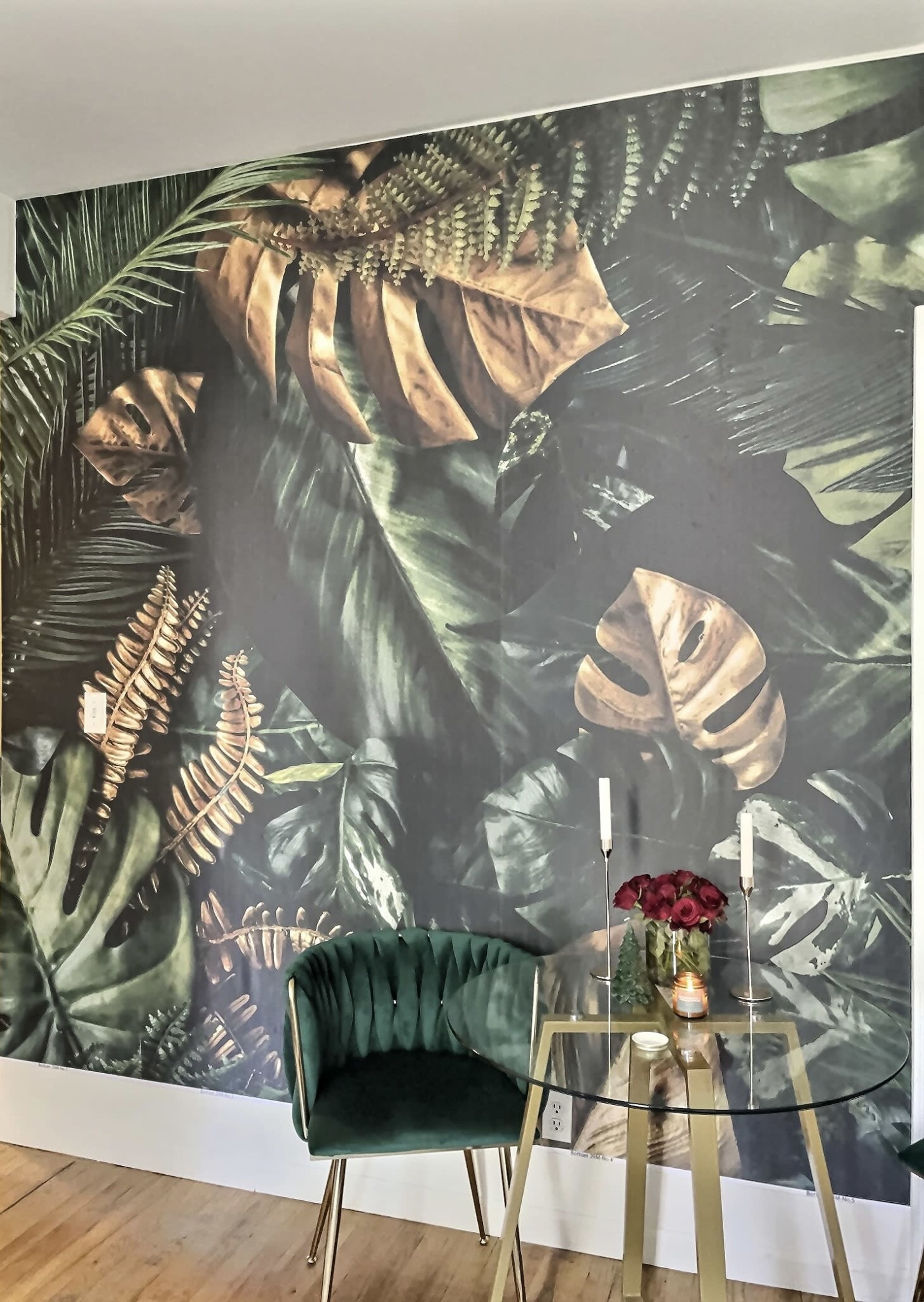 A room with a wall covered in a large, leafy green wallpaper, accompanied by a small glass table and a green chair.