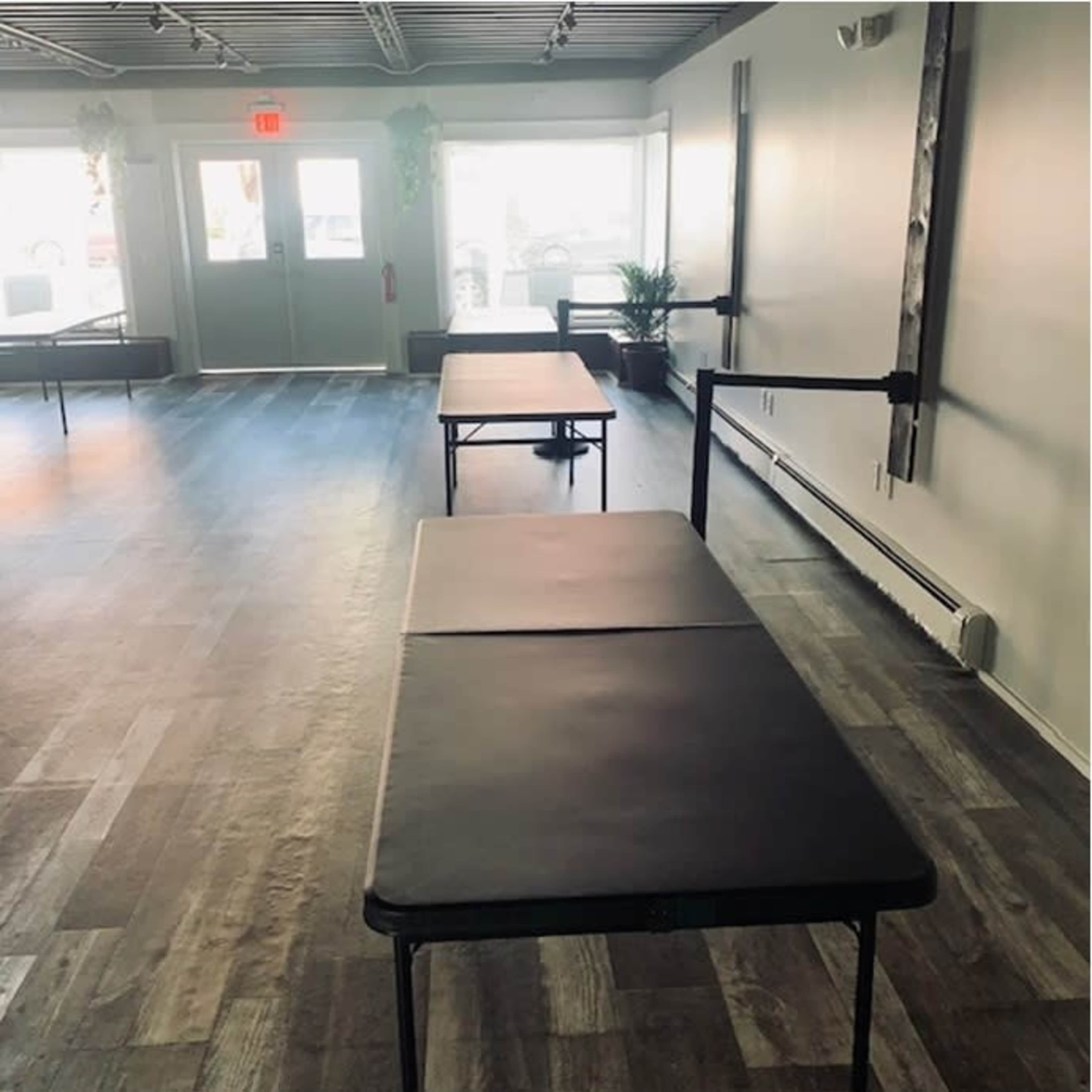 An interior space with two empty black folding tables arranged parallel to each other on a wooden floor.