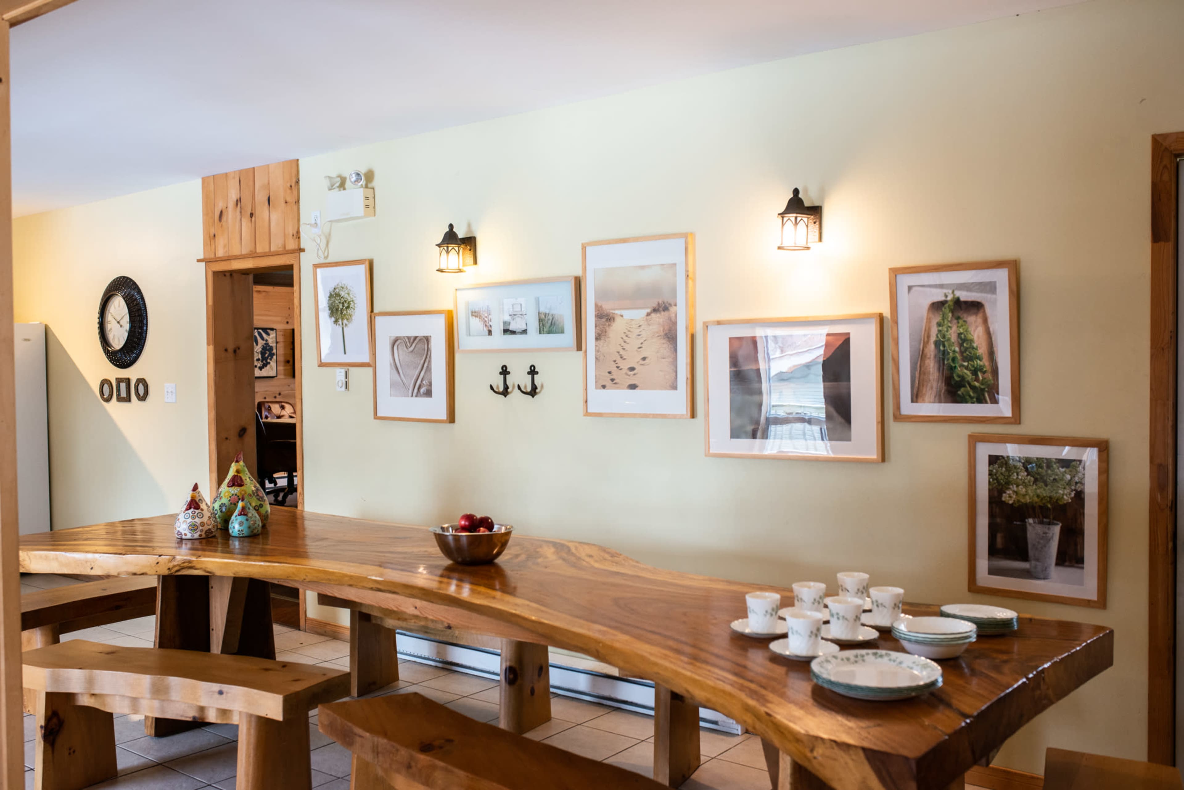 A wooden dining table with plates and cups set on it, surrounded by walls adorned with framed photographs and decorative items.