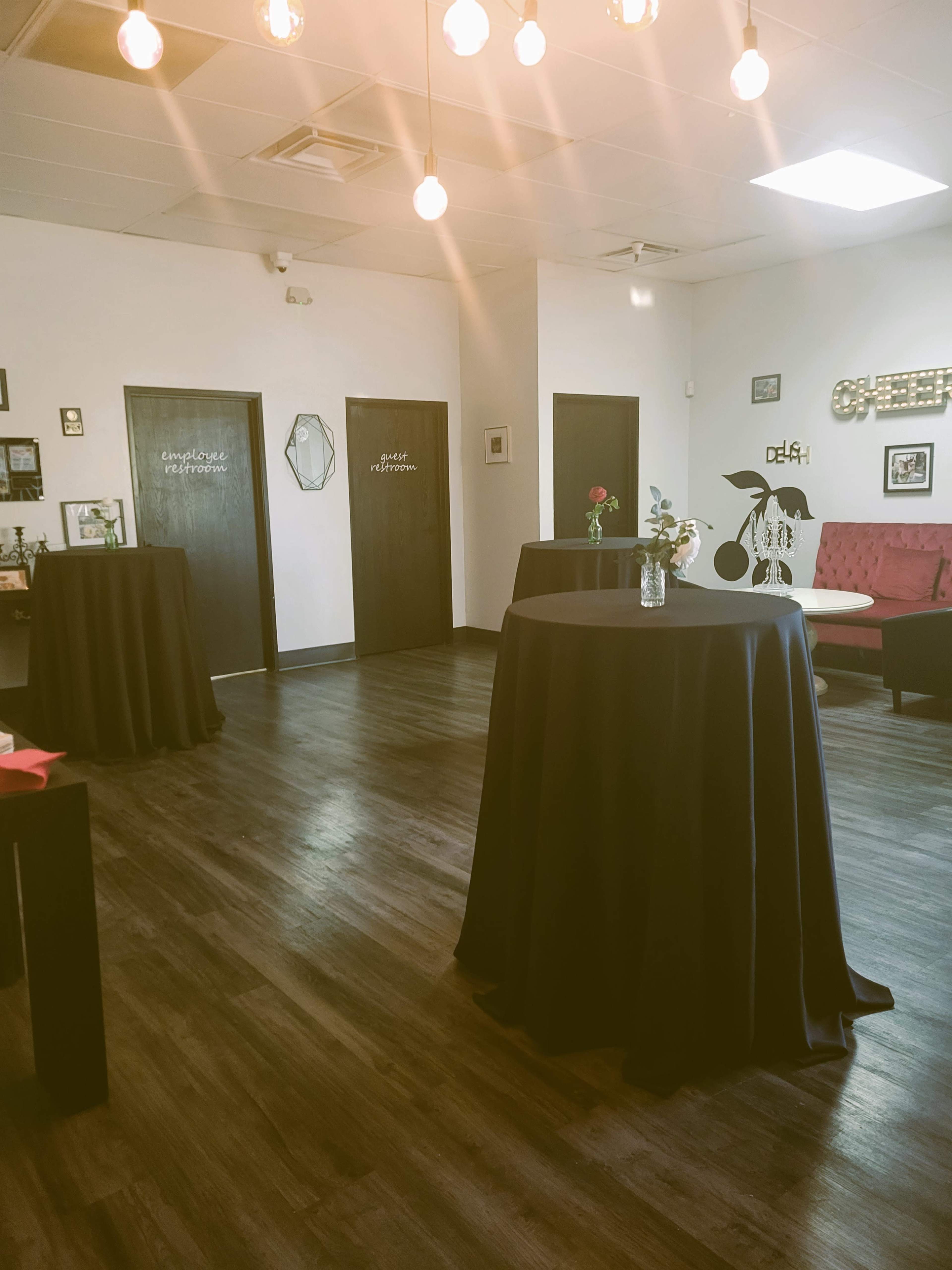 A modern, minimally furnished room with several high tables covered in black cloth, a red couch, and decorative elements on the walls.