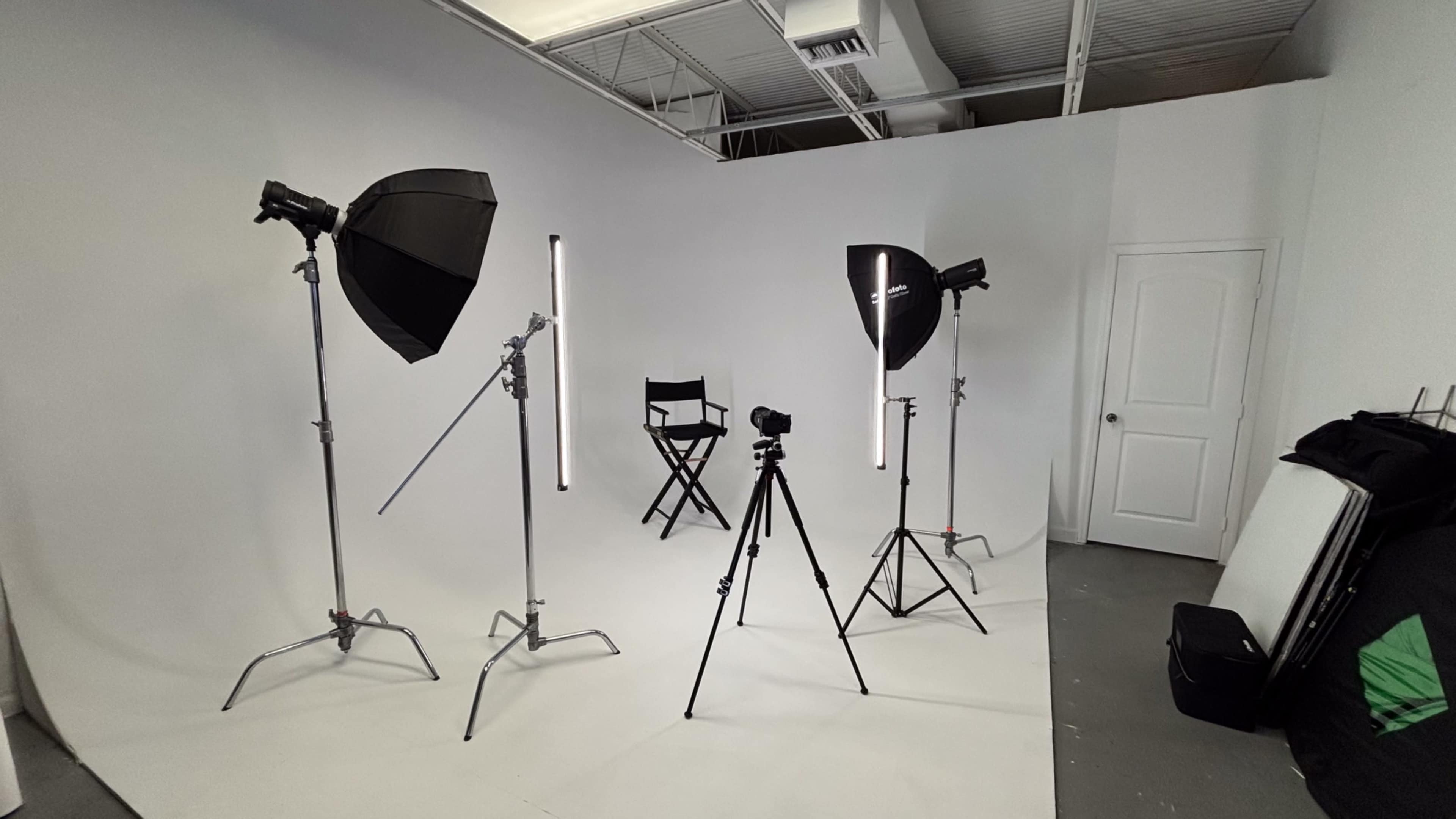 The image shows a photography studio setup with light stands, softboxes, a camera on a tripod, and a director's chair against a white backdrop.