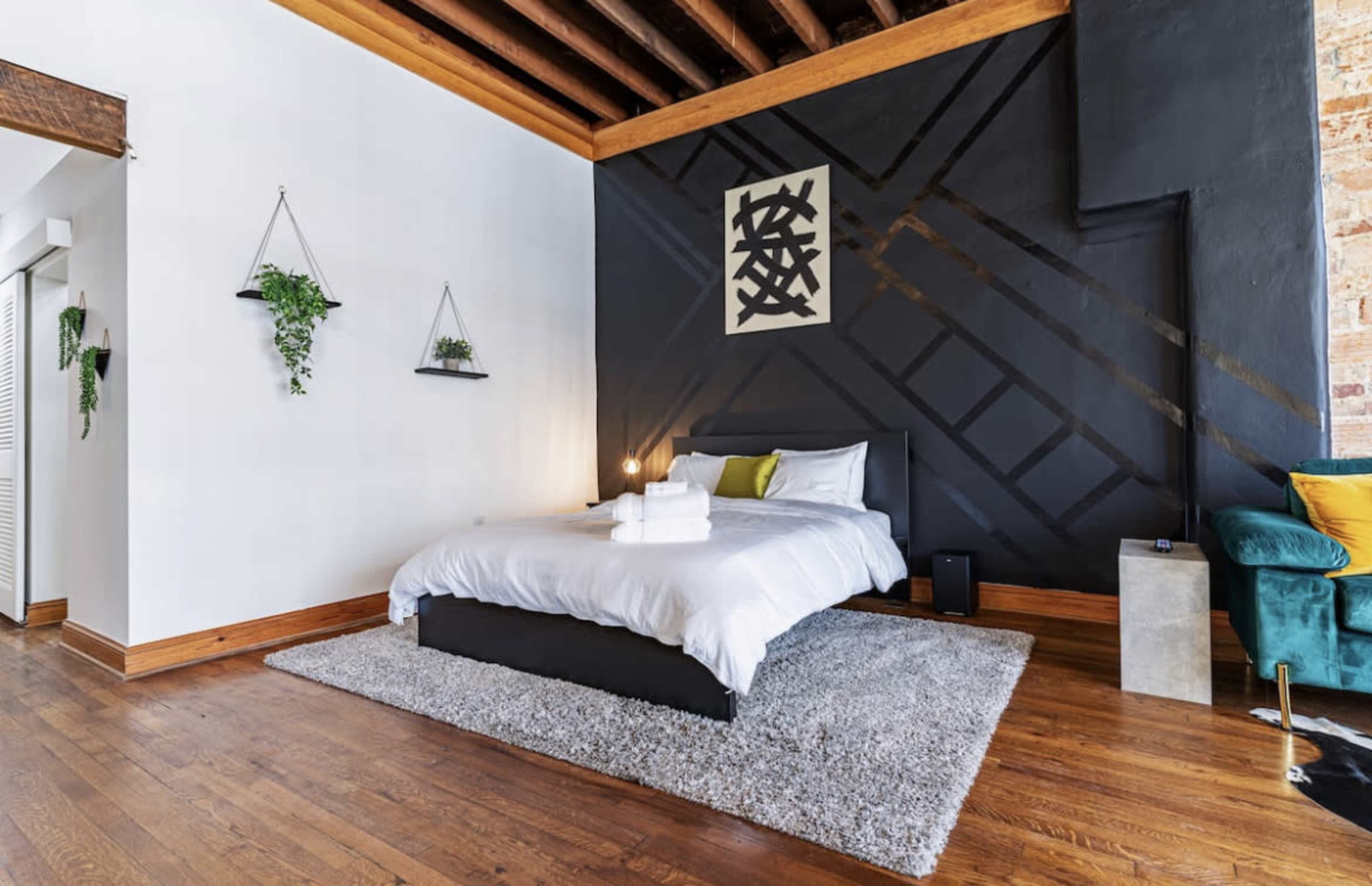 A modern bedroom with a black accent wall, a neatly made bed in the center, and a green velvet chair in the corner.