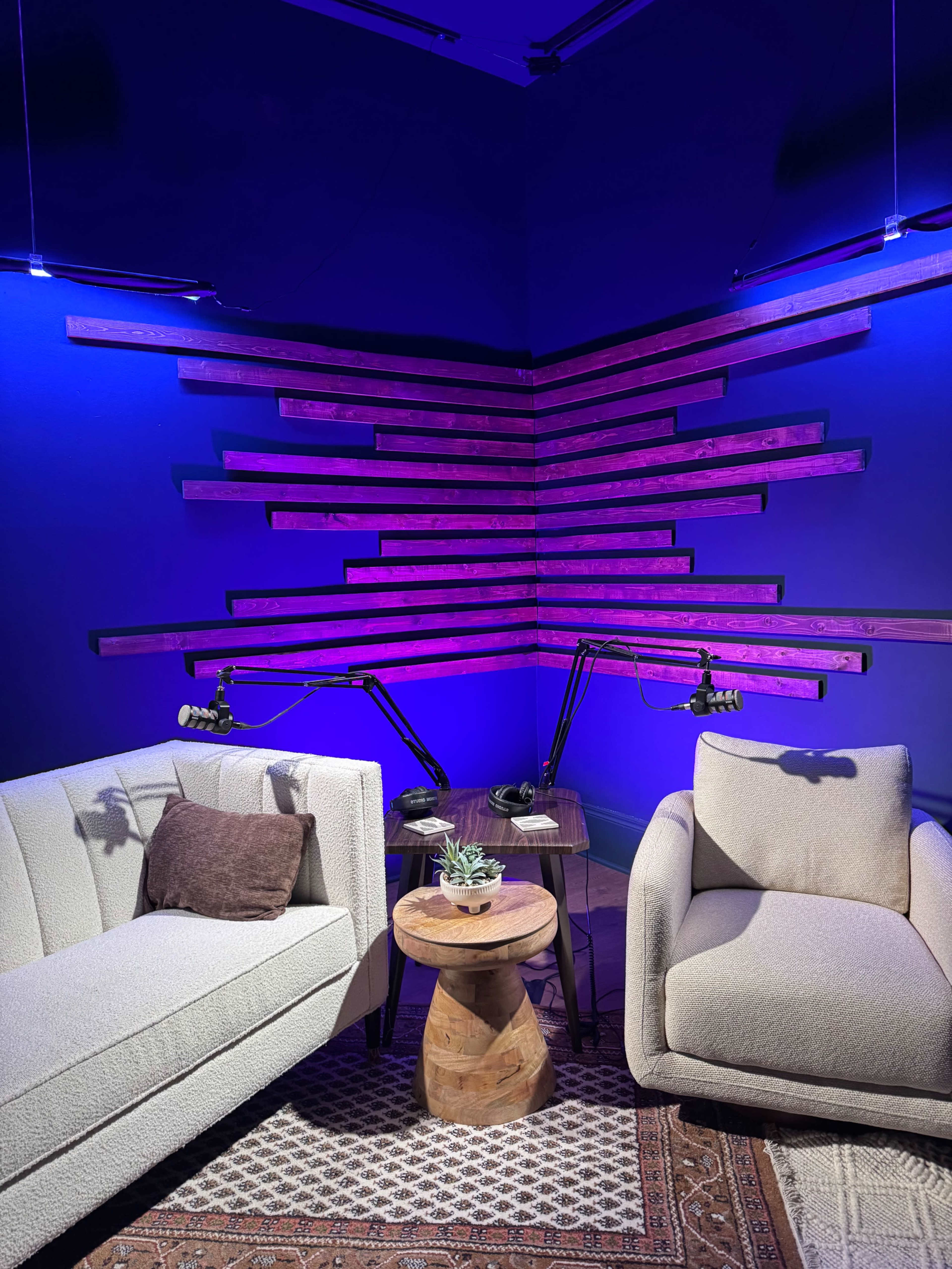 A cozy seating area features two armchairs and a small wooden table, with decorative lighting illuminating a wall of angled wooden strips.