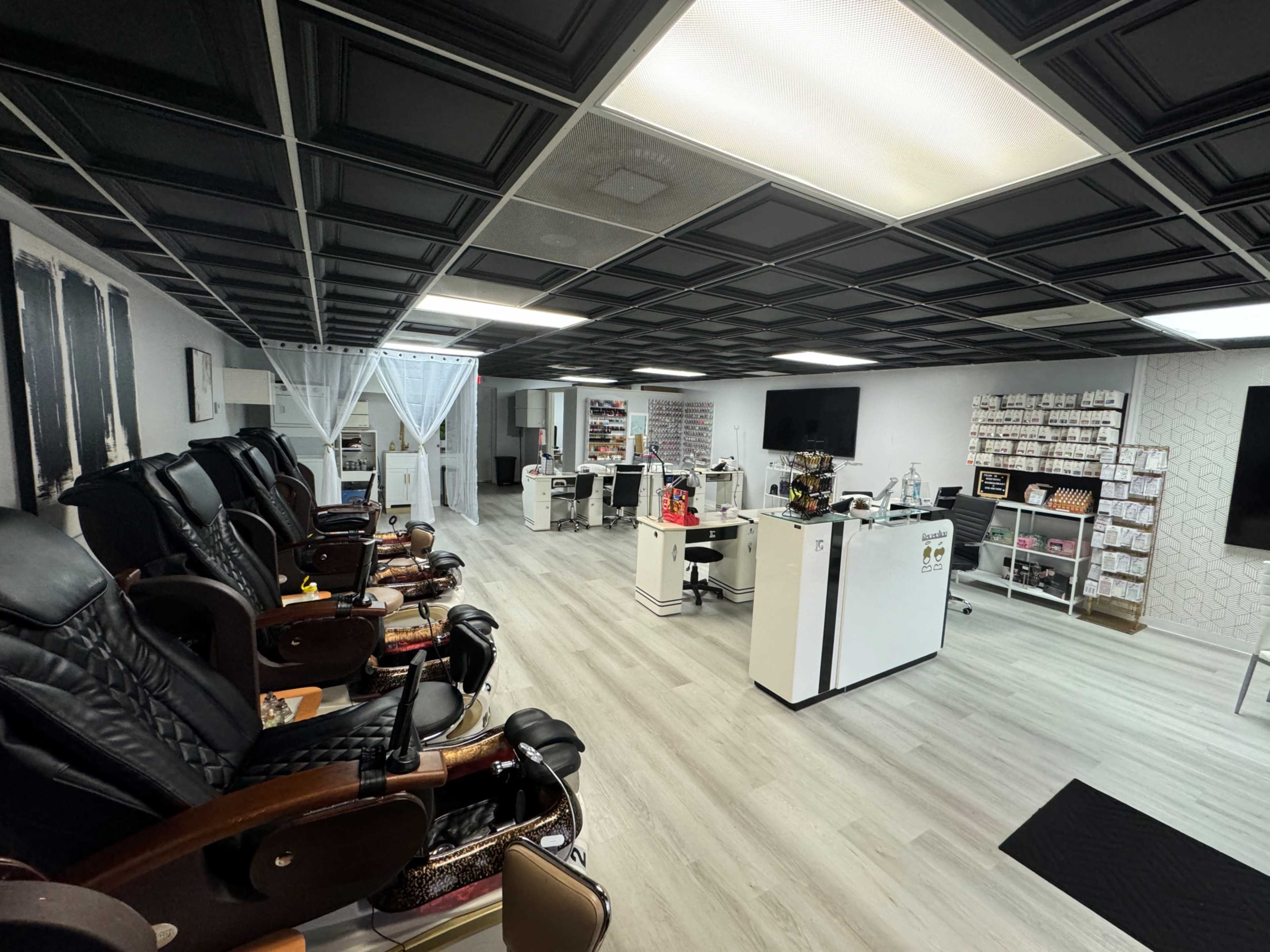 The image shows a spacious nail salon with several pedicure chairs on one side and treatment stations with a reception area on the other.