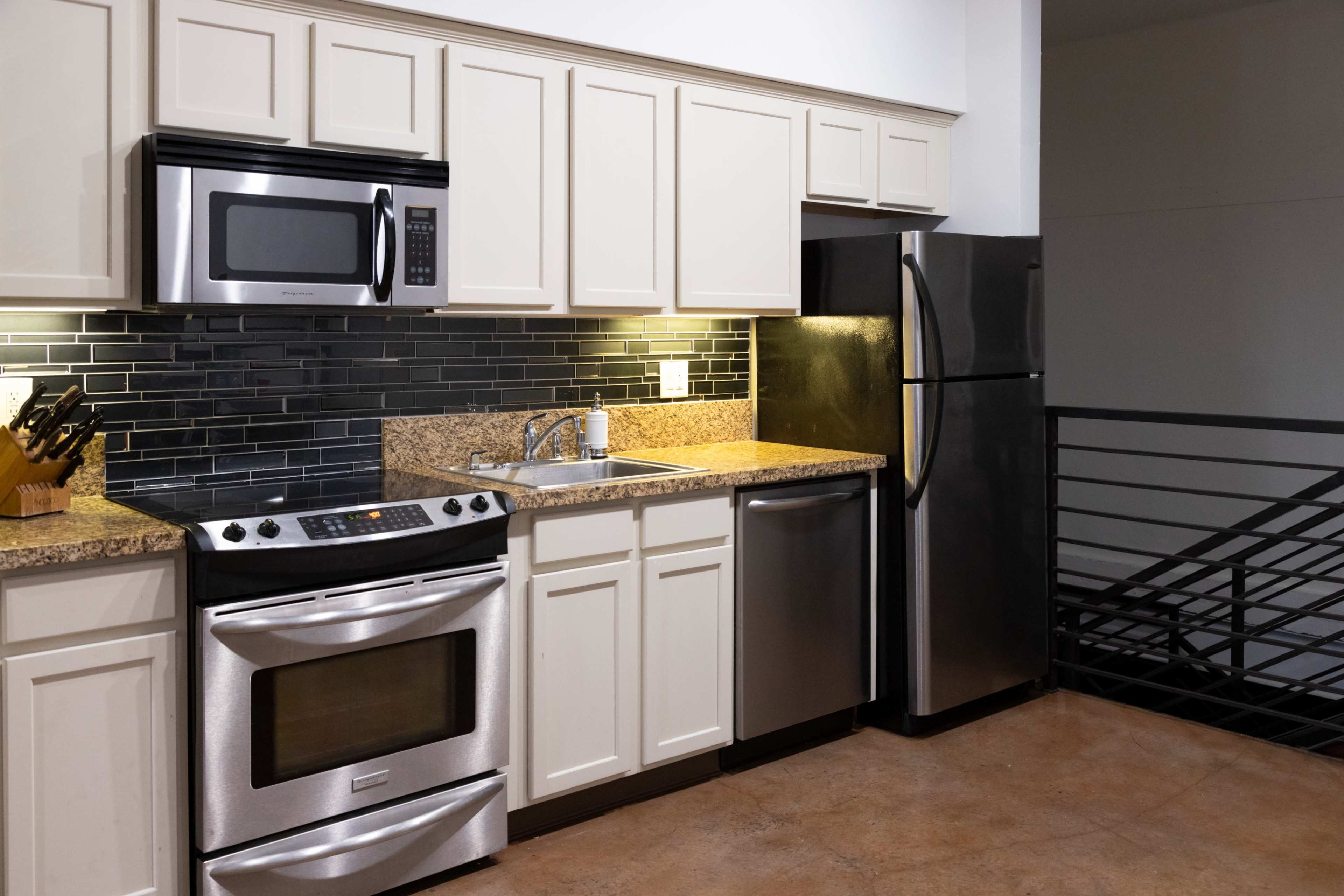 The kitchen features stainless steel appliances, including a refrigerator, oven, and microwave, along with granite countertops and dark tiled backsplash.