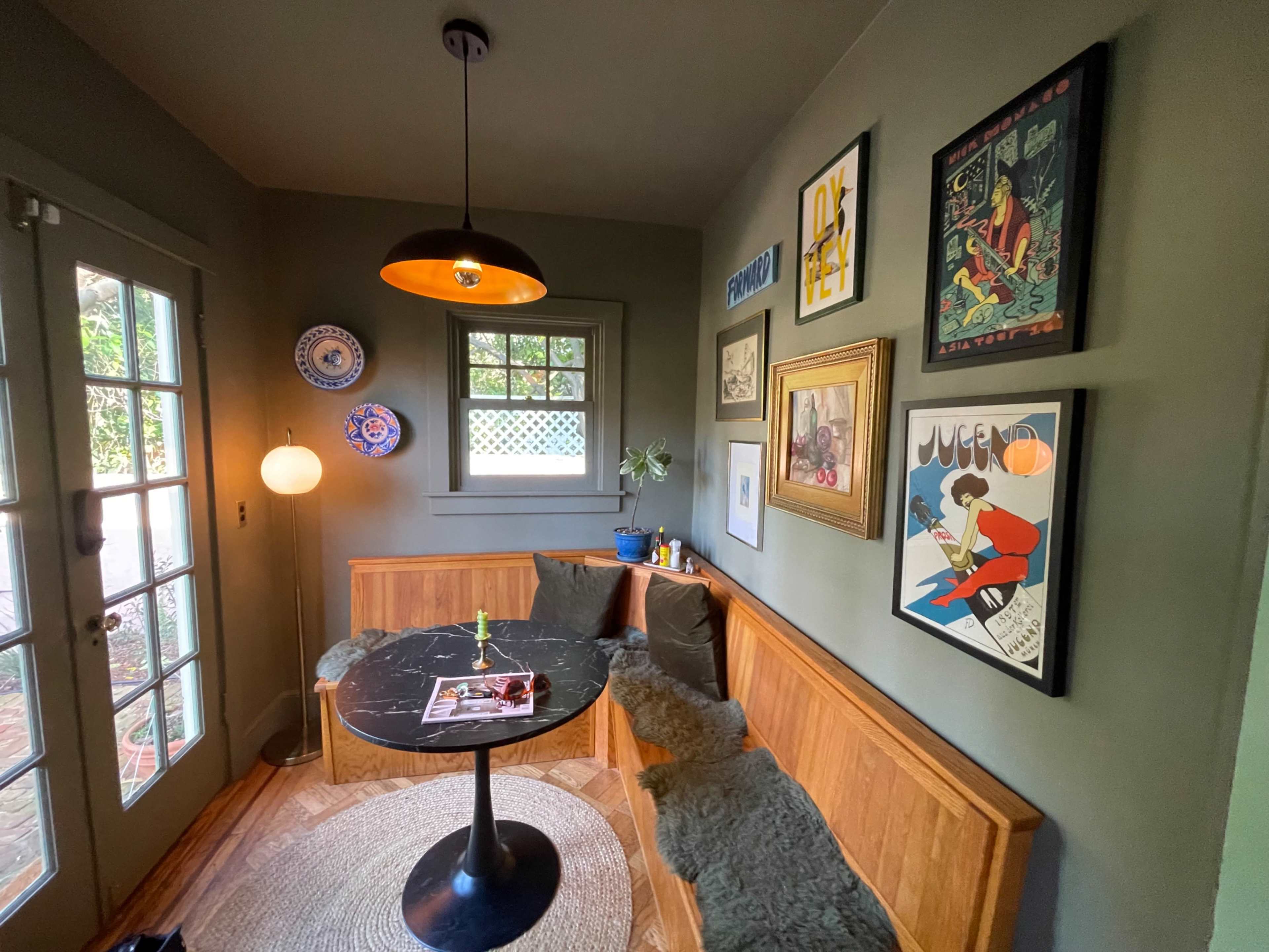 The image shows a cozy corner in a room with a round black table, wooden bench seating, and various framed artworks on the walls.