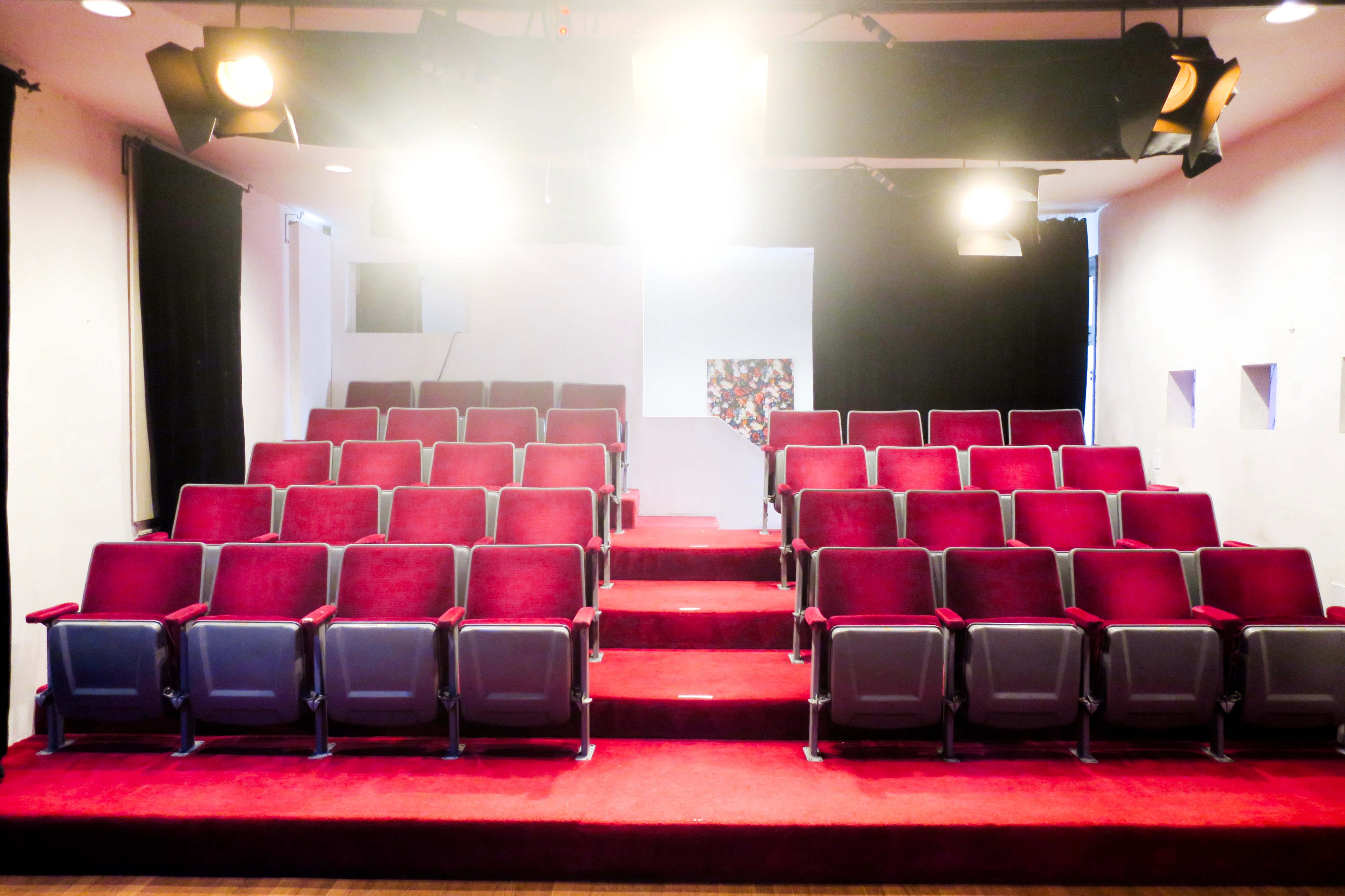 A seating area in a small theater, featuring rows of burgundy chairs arranged on a raised red carpet.