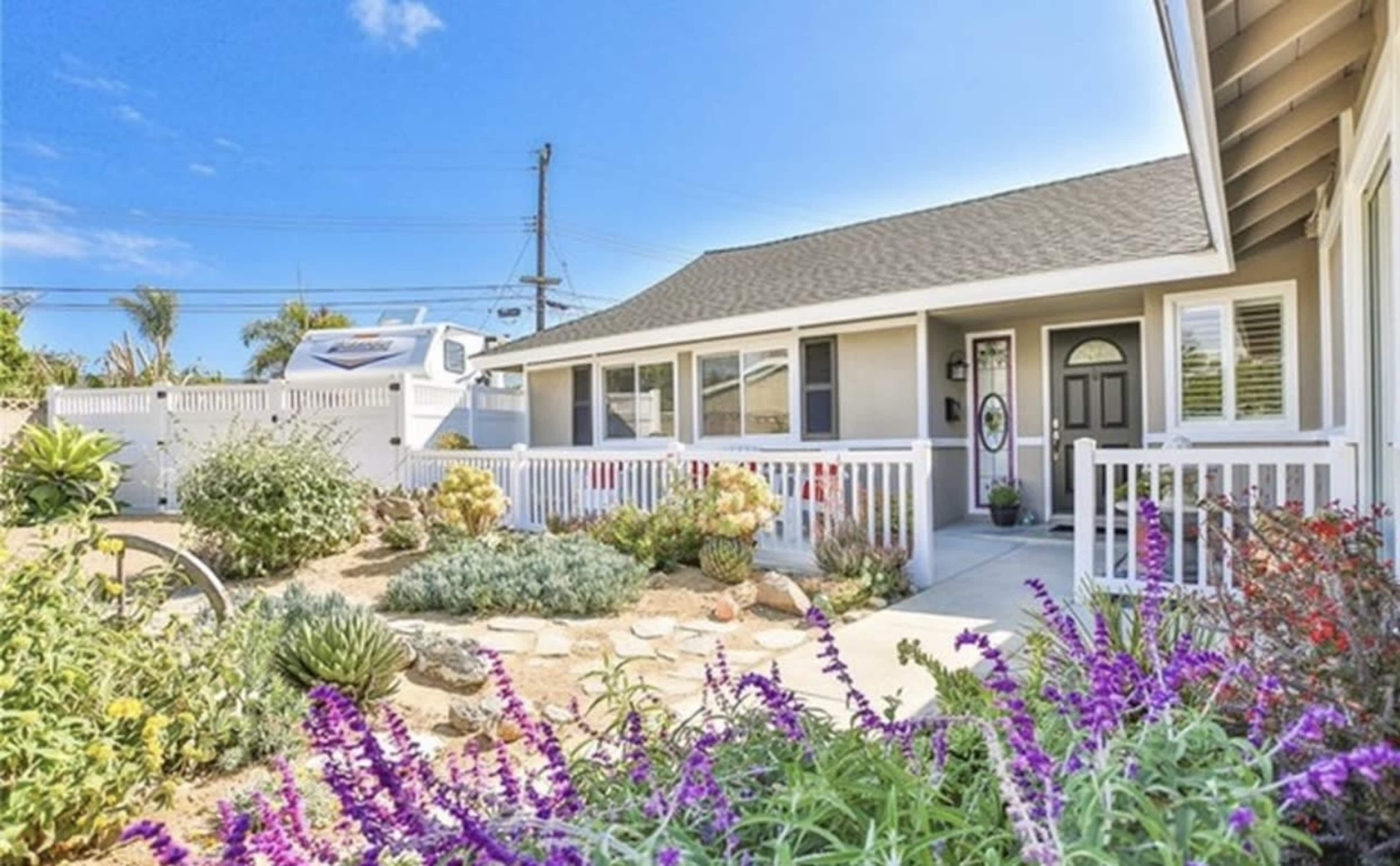 A residential house with a front yard featuring a pathway, various plants, and colorful flowers.