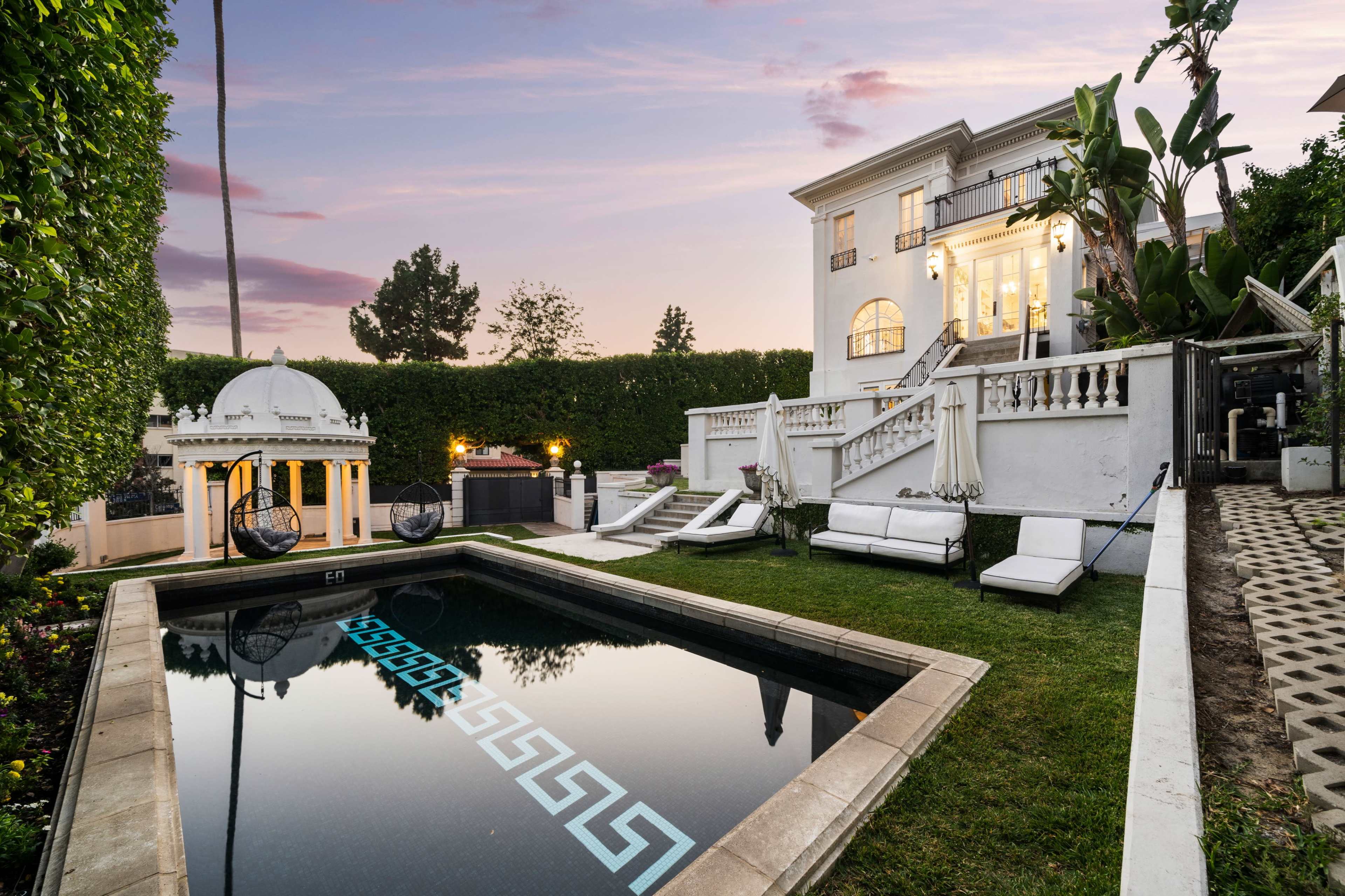 The image shows a luxury villa with a swimming pool surrounded by well-manicured landscaping and outdoor seating areas.