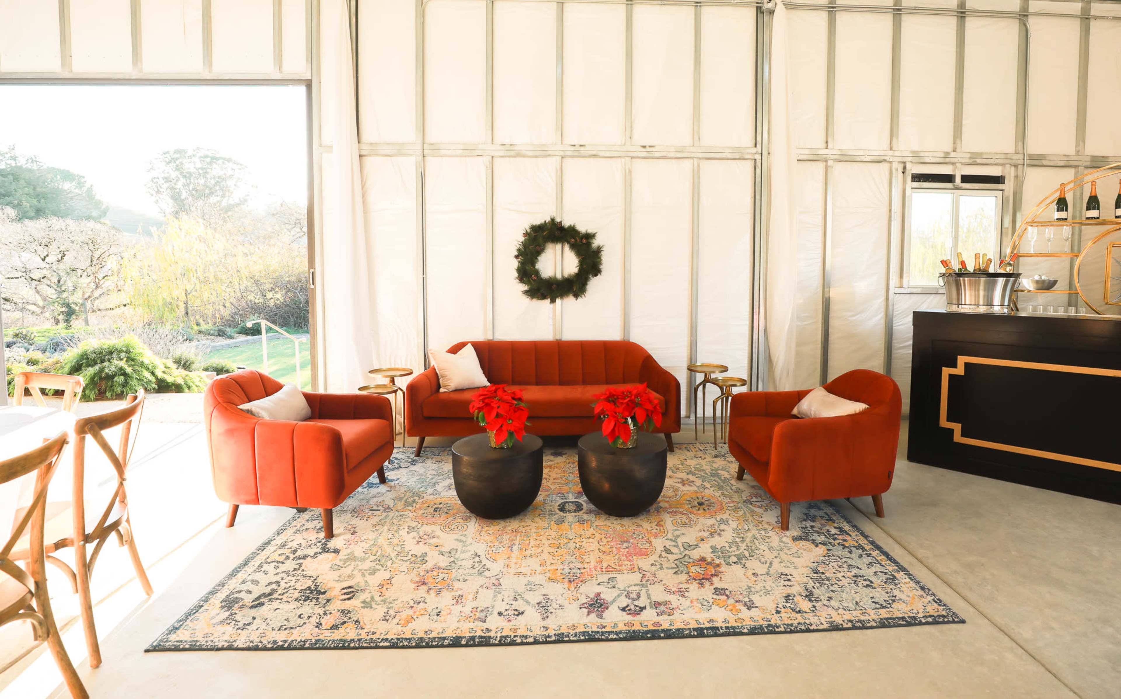 A modern lounge area features a red sofa and chairs around a patterned rug, with a black bar and festive decorations.