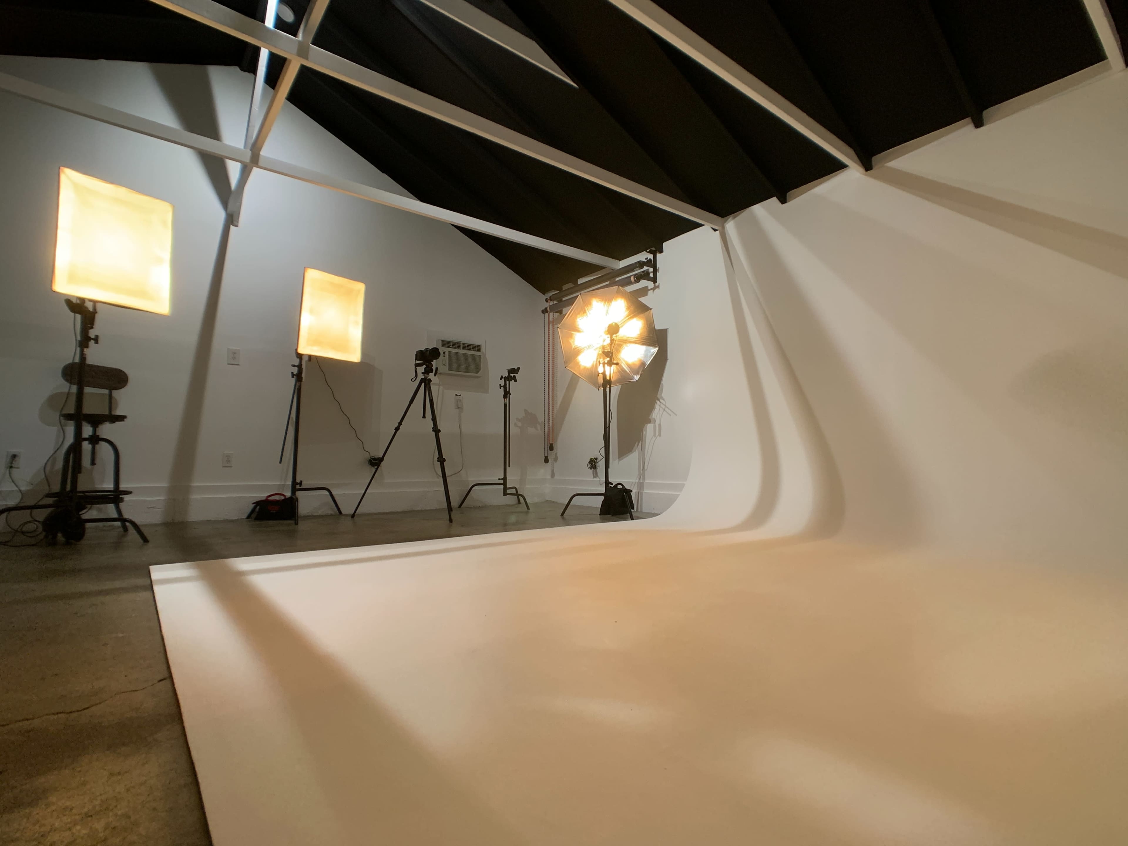 A photography studio with softbox lights and a backdrop set against a plain wall.
