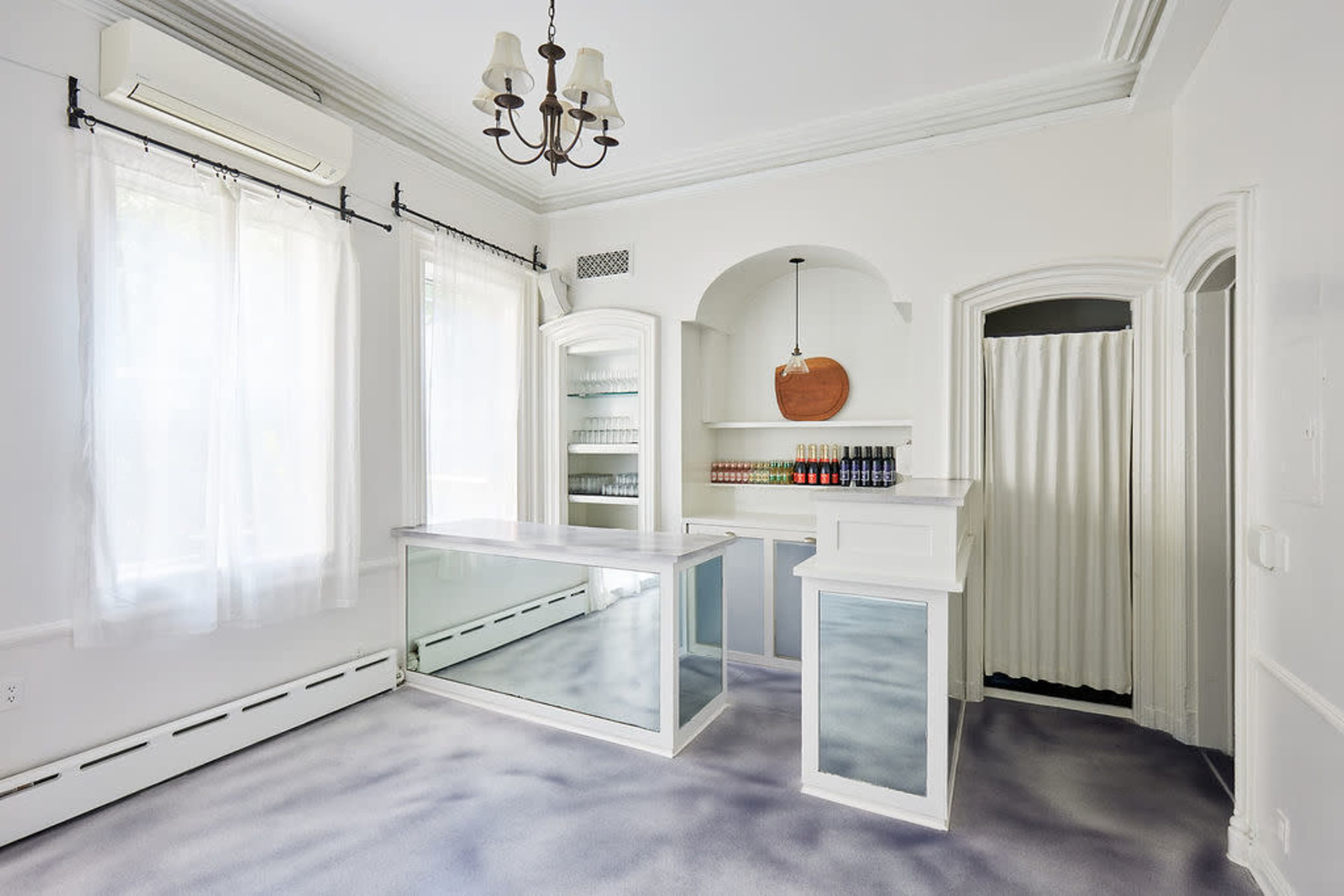 The image shows a bright interior space featuring a reception area with a glass counter, shelves lined with products, and an adjacent room separated by a curtain.
