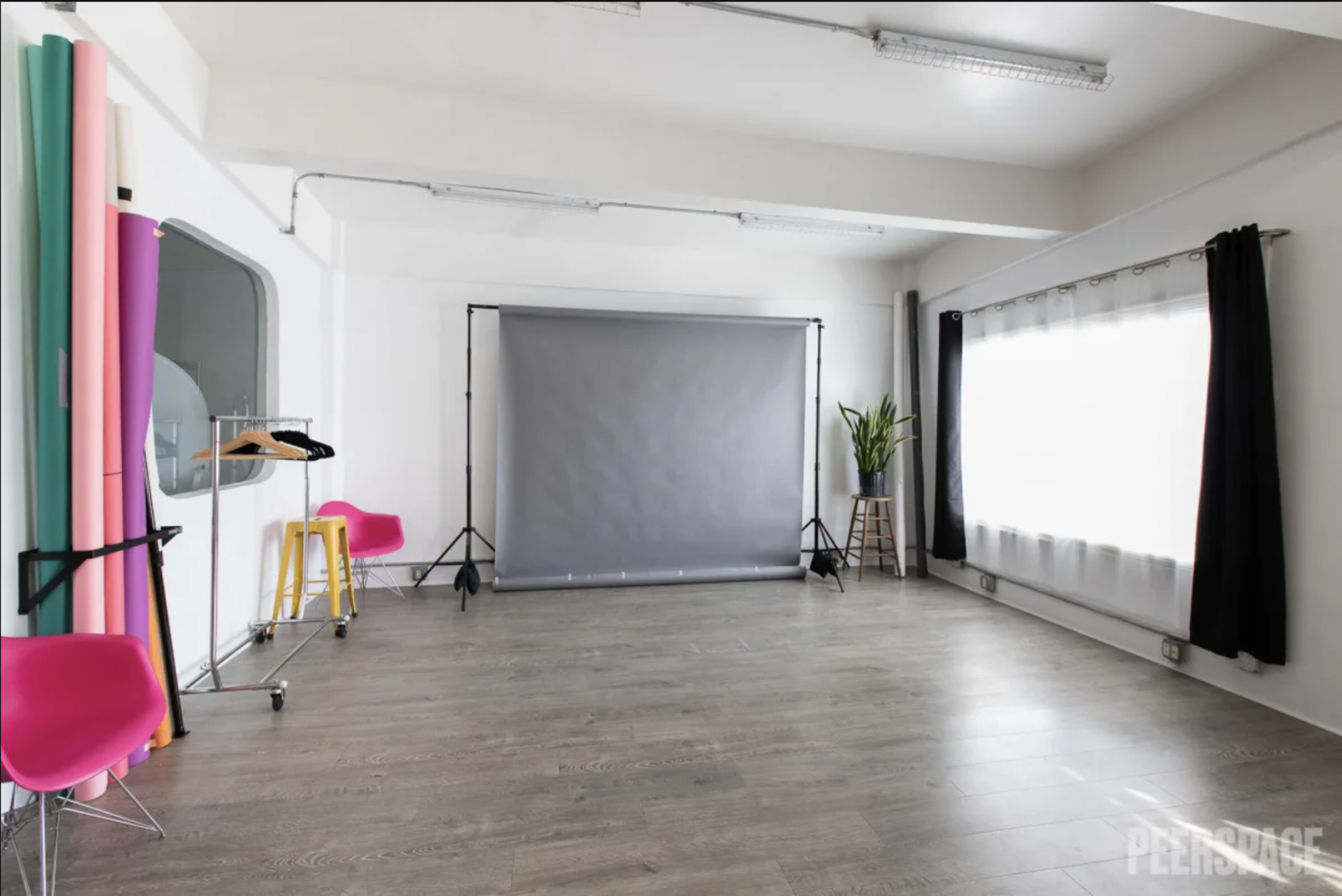 A photography studio with a gray backdrop, colorful paper rolls, and modern furniture arranged in a well-lit space.