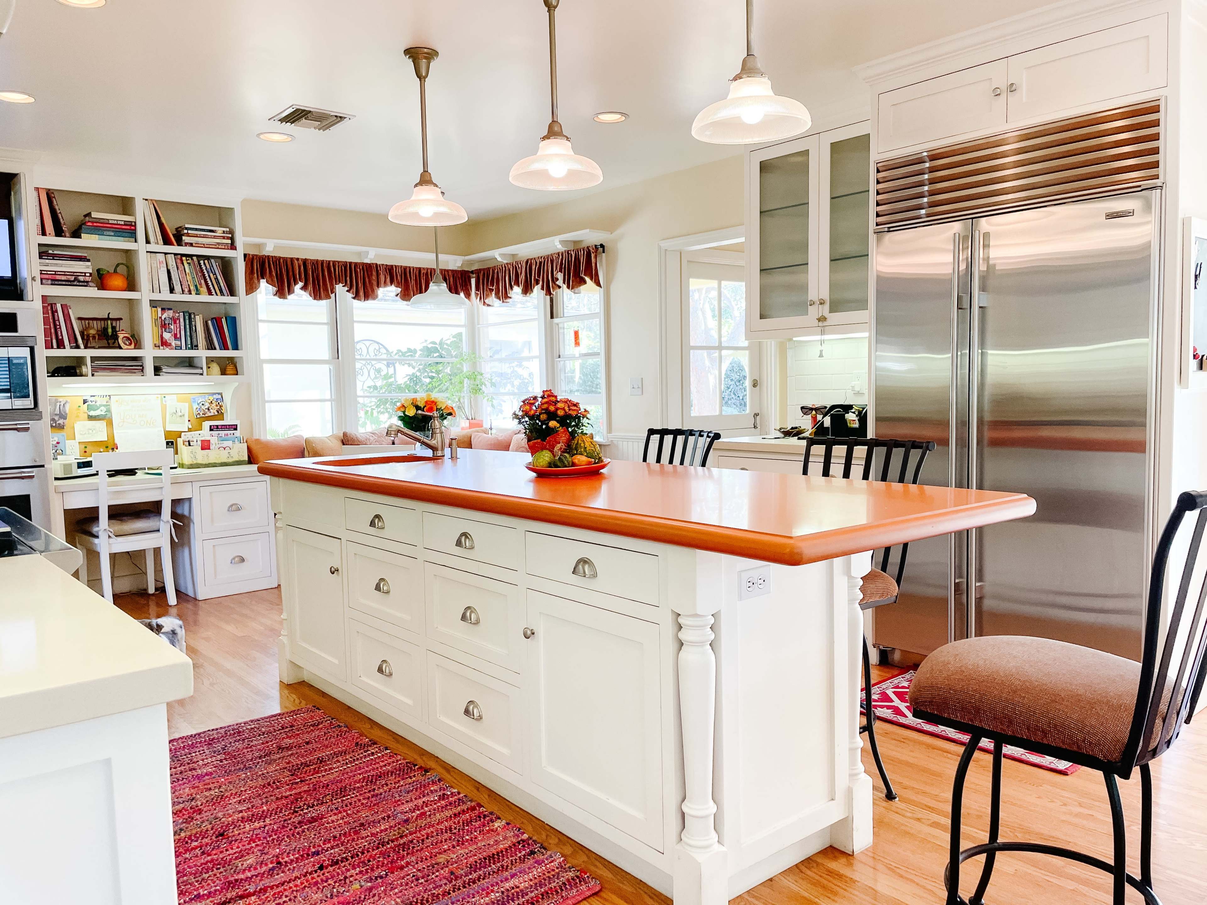 A bright kitchen features a central island with a wooden countertop, white cabinetry, and stainless steel appliances.
