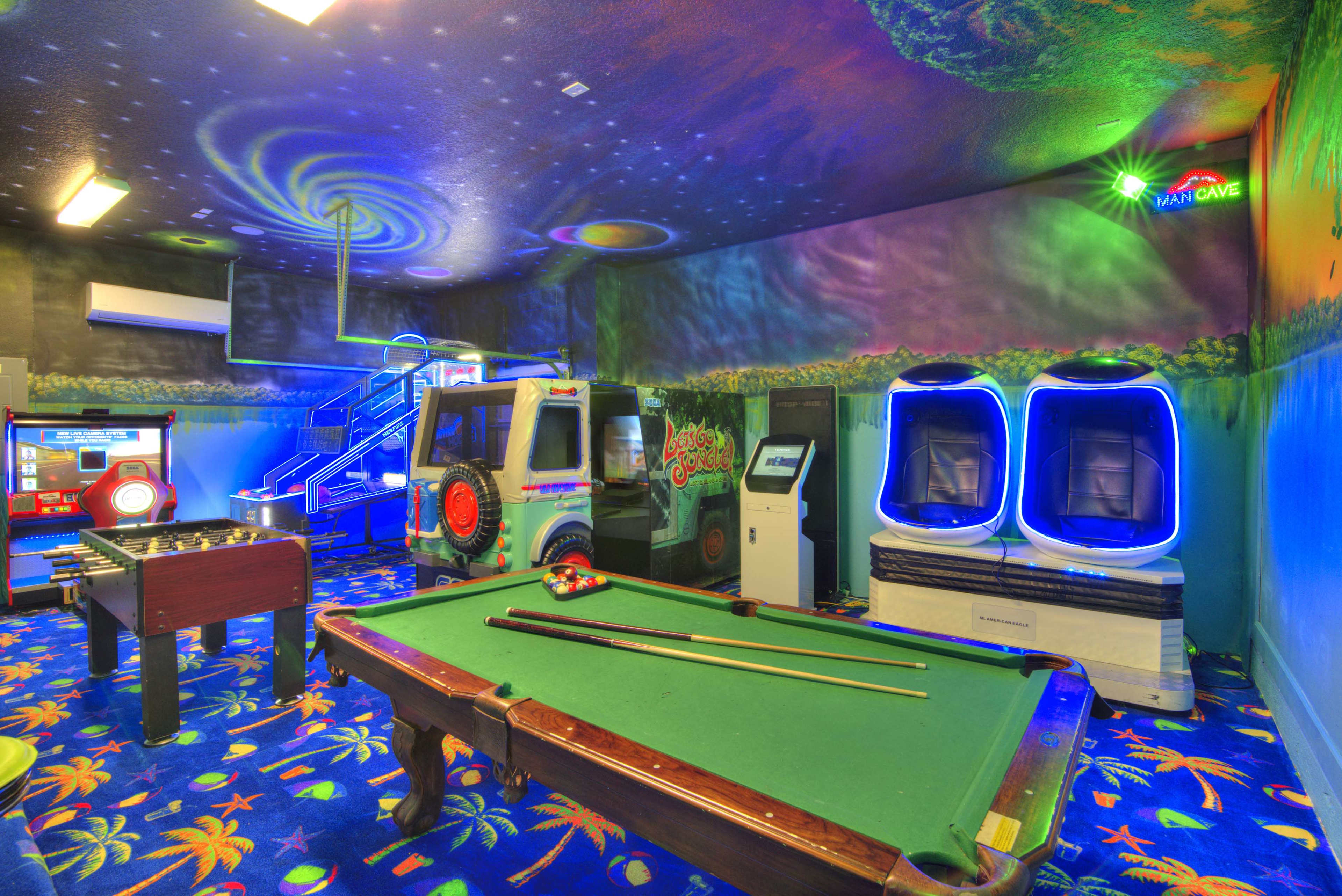 The image shows a vibrant game room featuring a pool table, arcade machines, and colorful decor with a cosmic theme on the walls and ceiling.