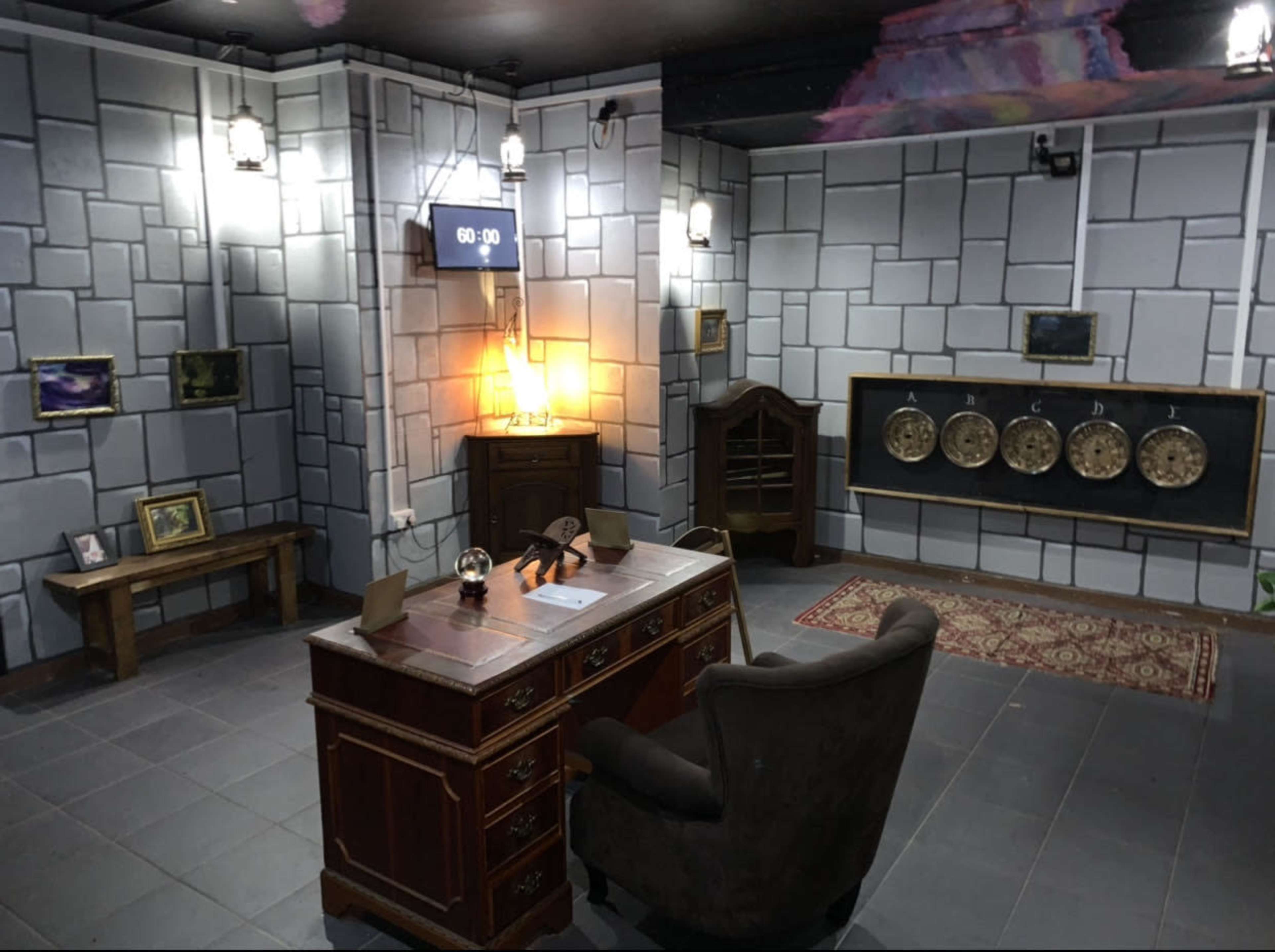 A room designed like an escape room, featuring a wooden desk with a chair, a wall clock counting down from 60:00, and various decorative elements on the stone-patterned walls.