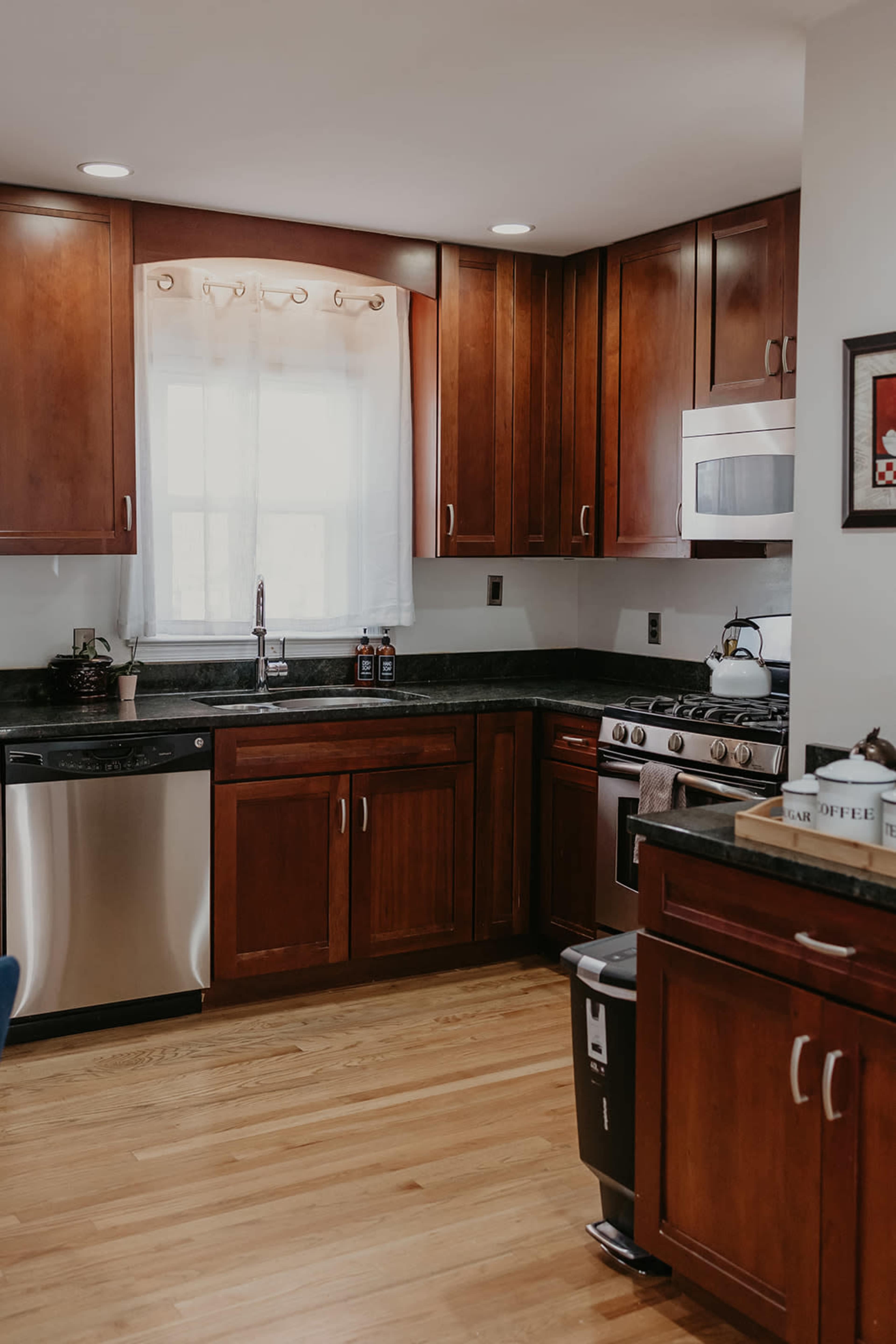The kitchen features wooden cabinetry, a stainless steel dishwasher, and a black countertop with an oven and a microwave.