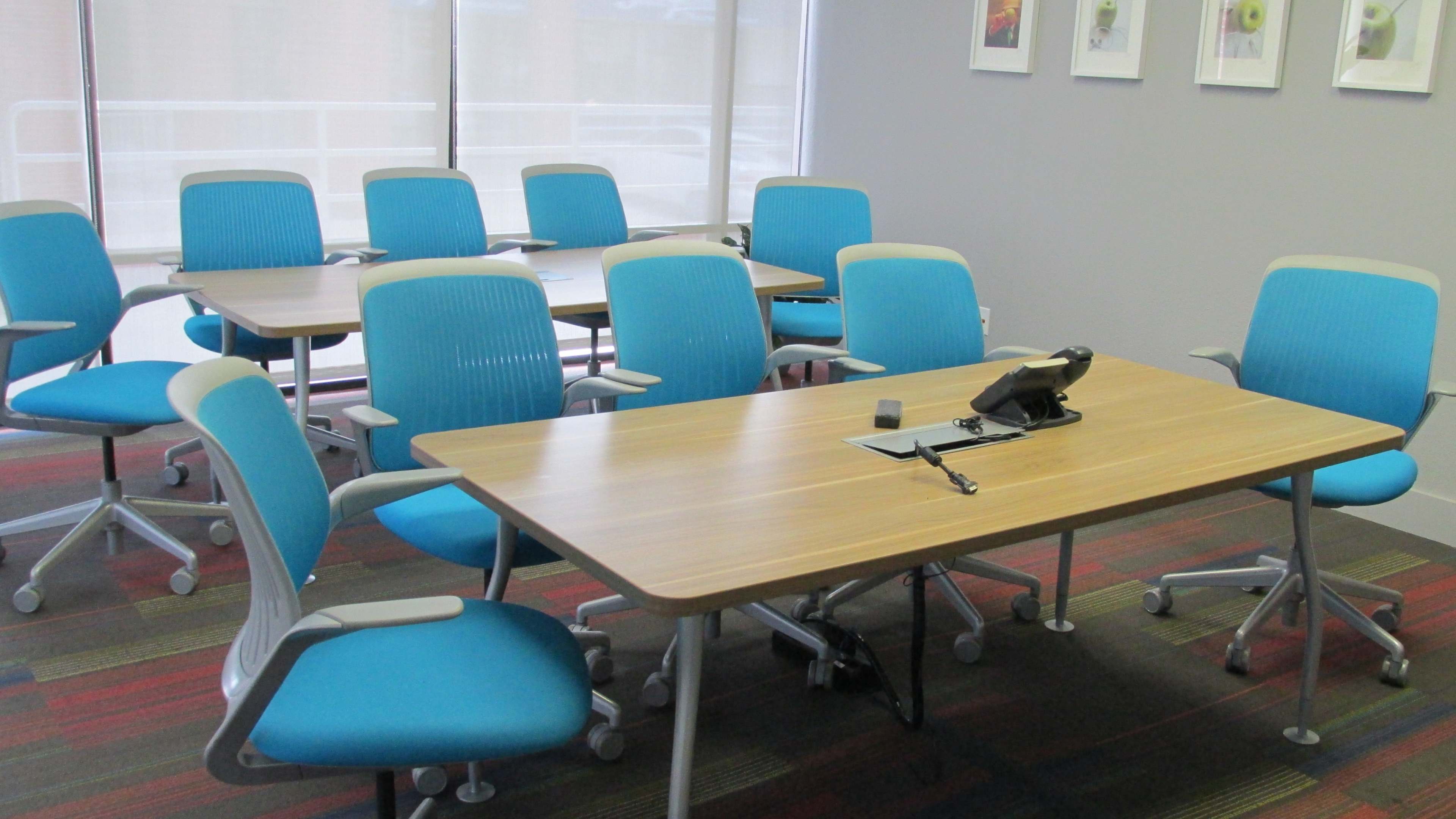 A conference room with multiple blue chairs arranged around wooden tables and a telephone on one of the tables.