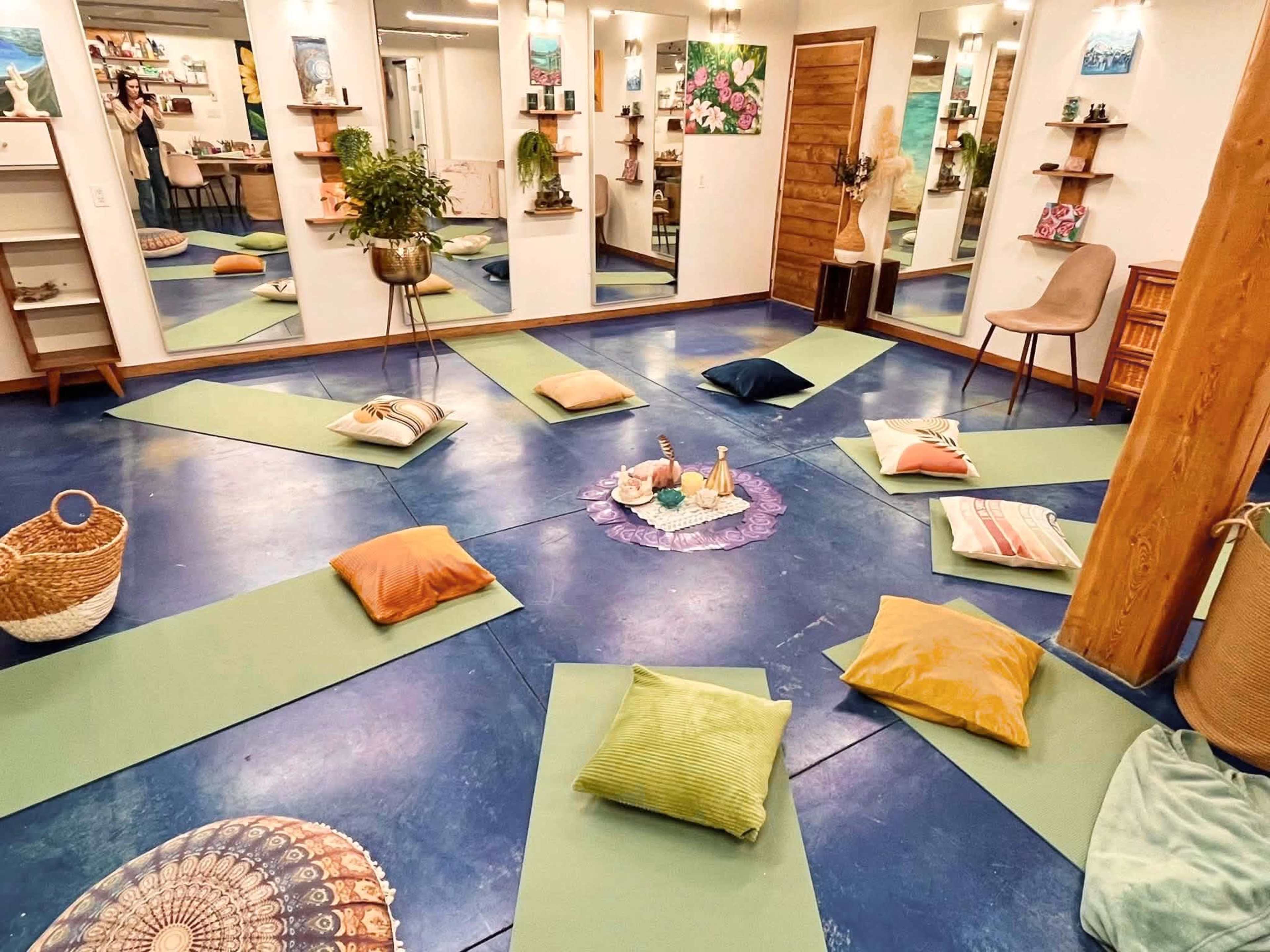 The image shows a wellness studio with yoga mats arranged in a circular pattern around a decorative centerpiece, and mirrors reflecting the space.