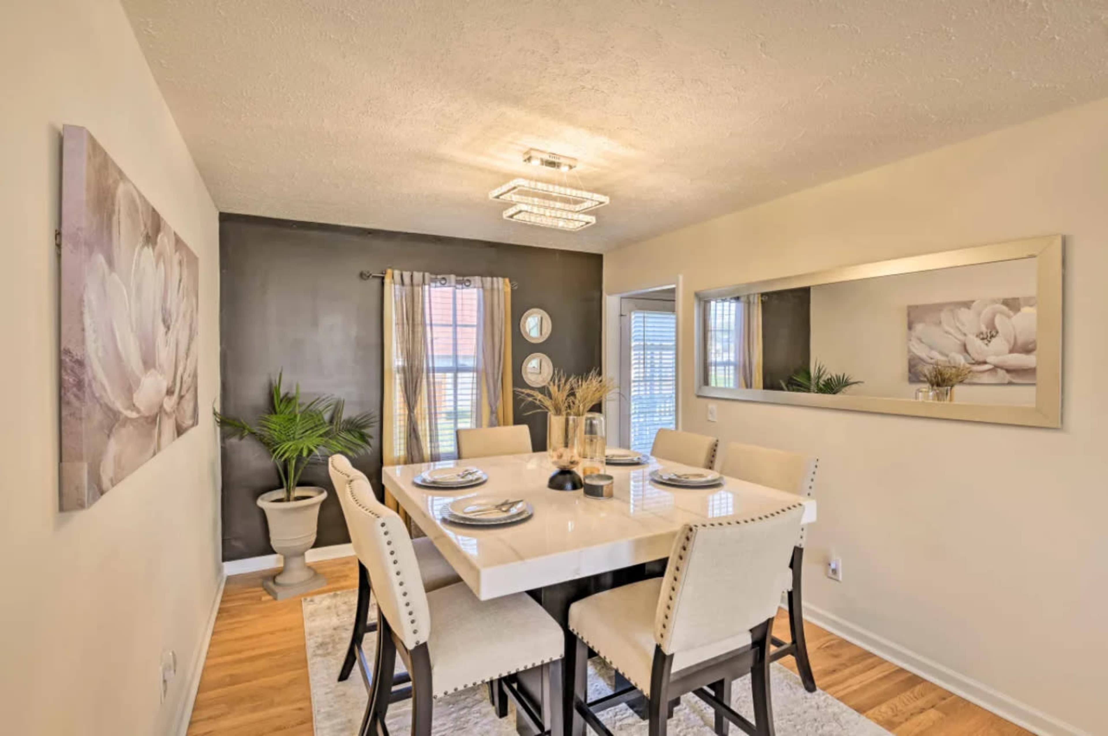 A modern dining room features a square table set for six, with a decorative mirror and artwork on the walls.