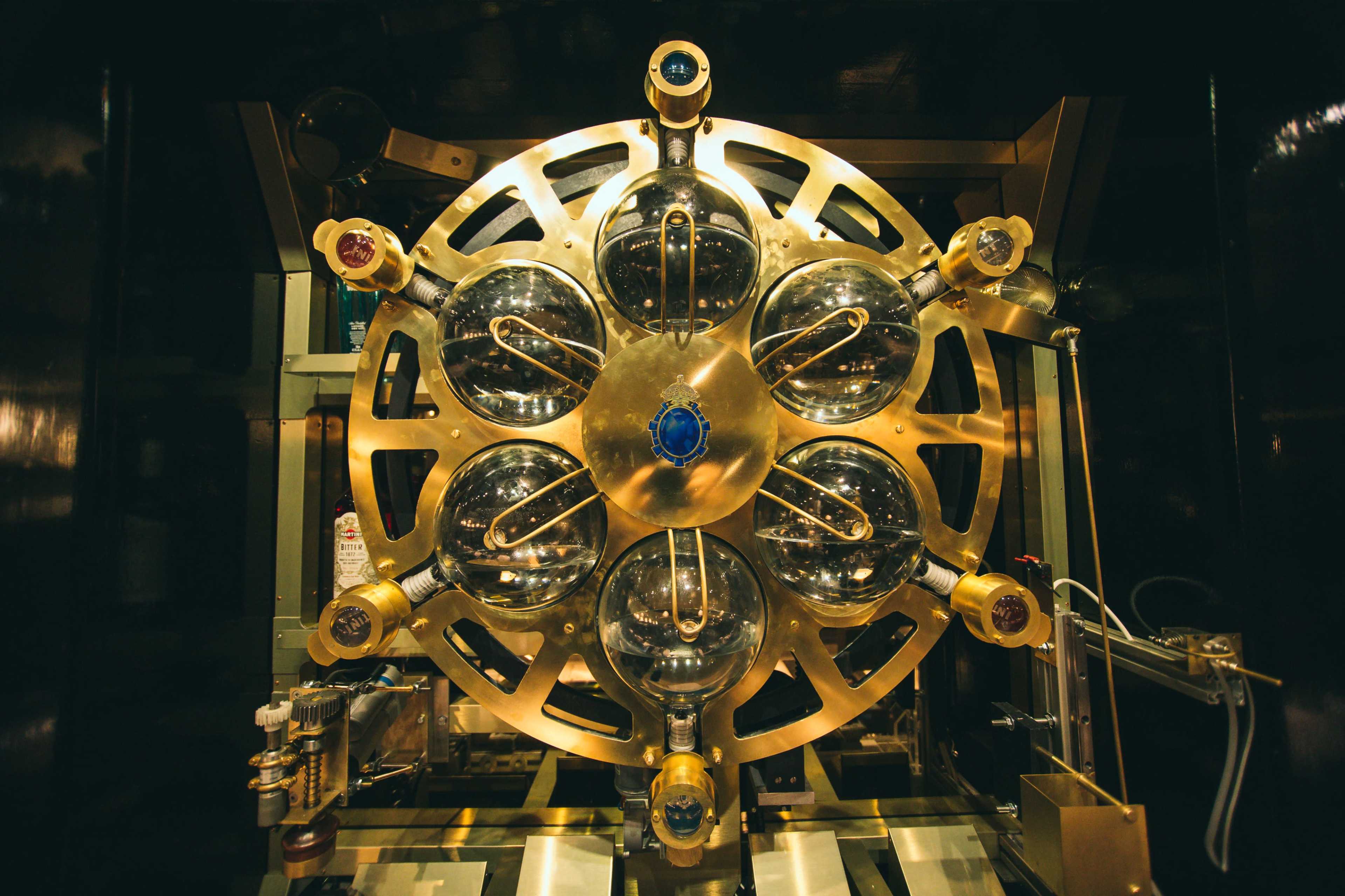 The image shows a large, circular machine with multiple glass chambers and metallic connectors arranged in a symmetrical design.