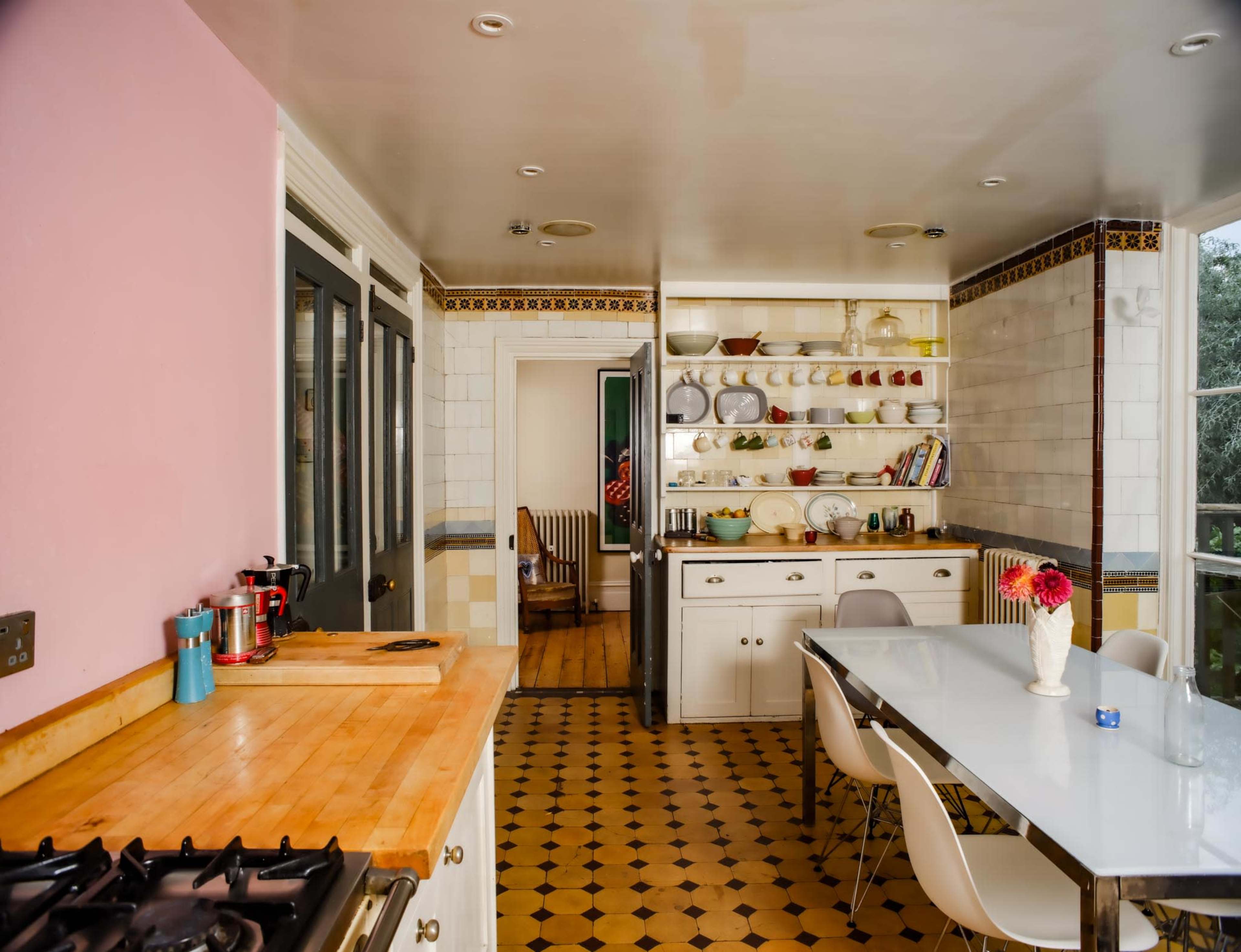 A modern kitchen features a wooden countertop, a gas stove, open shelving with dishes, and a dining table with white chairs.