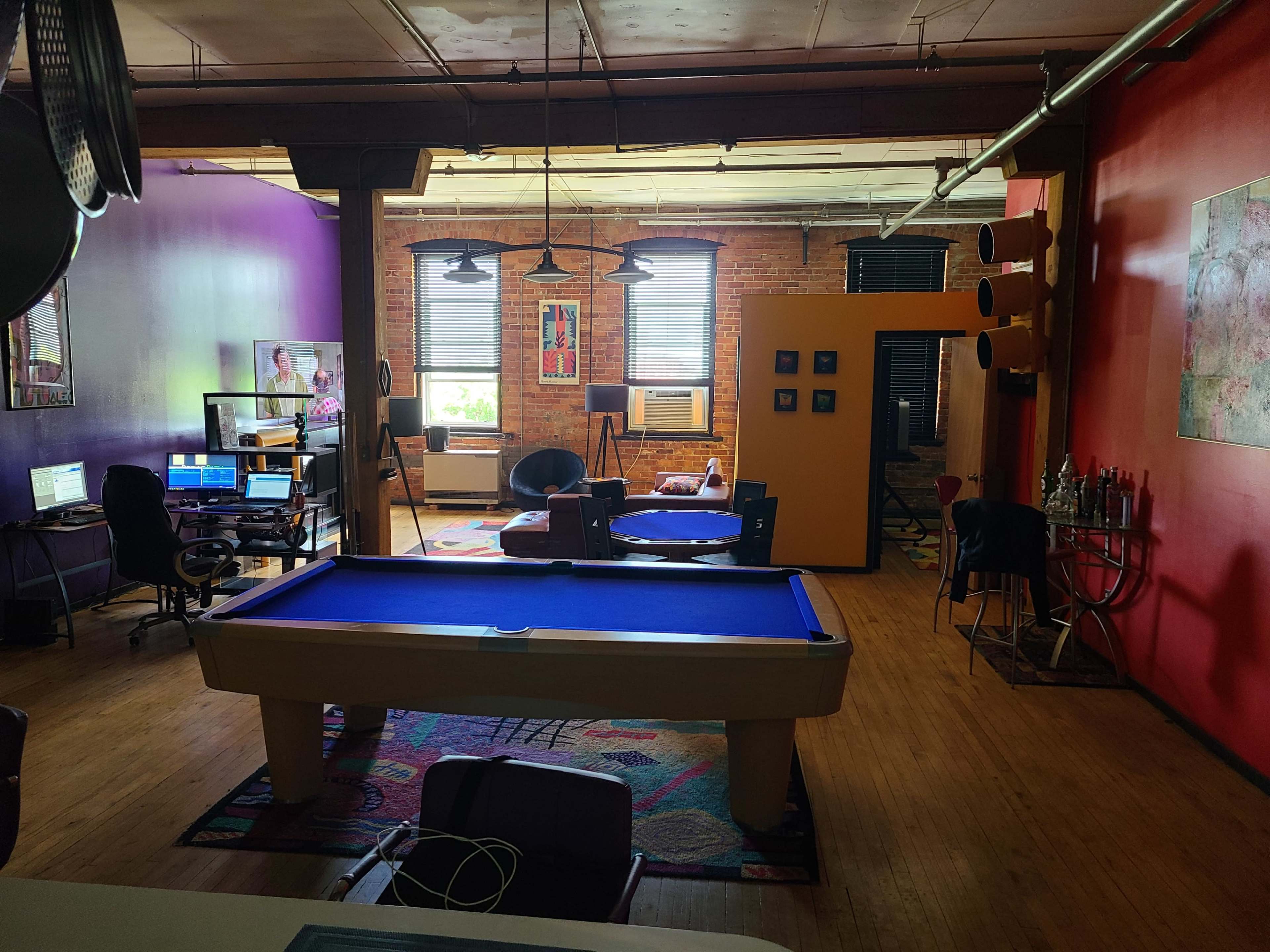 A spacious room with a pool table, desks with computers, and colorful walls in an industrial-style setting.
