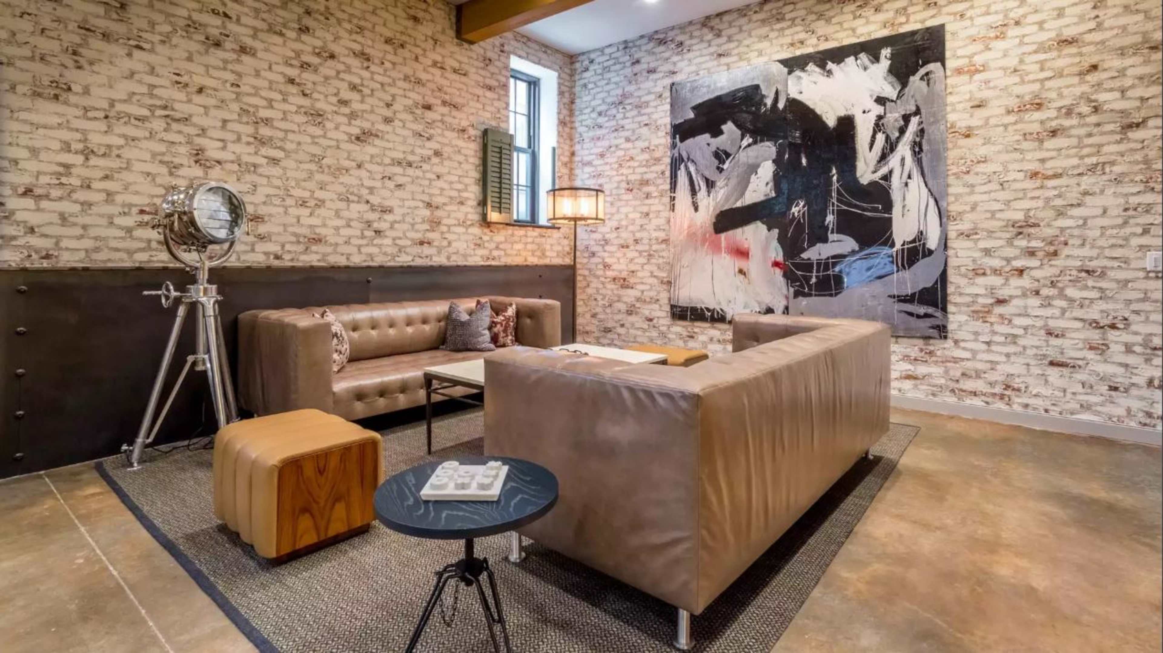 A modern lounge area featuring two leather sofas, a side table, and a large abstract painting on a brick wall.