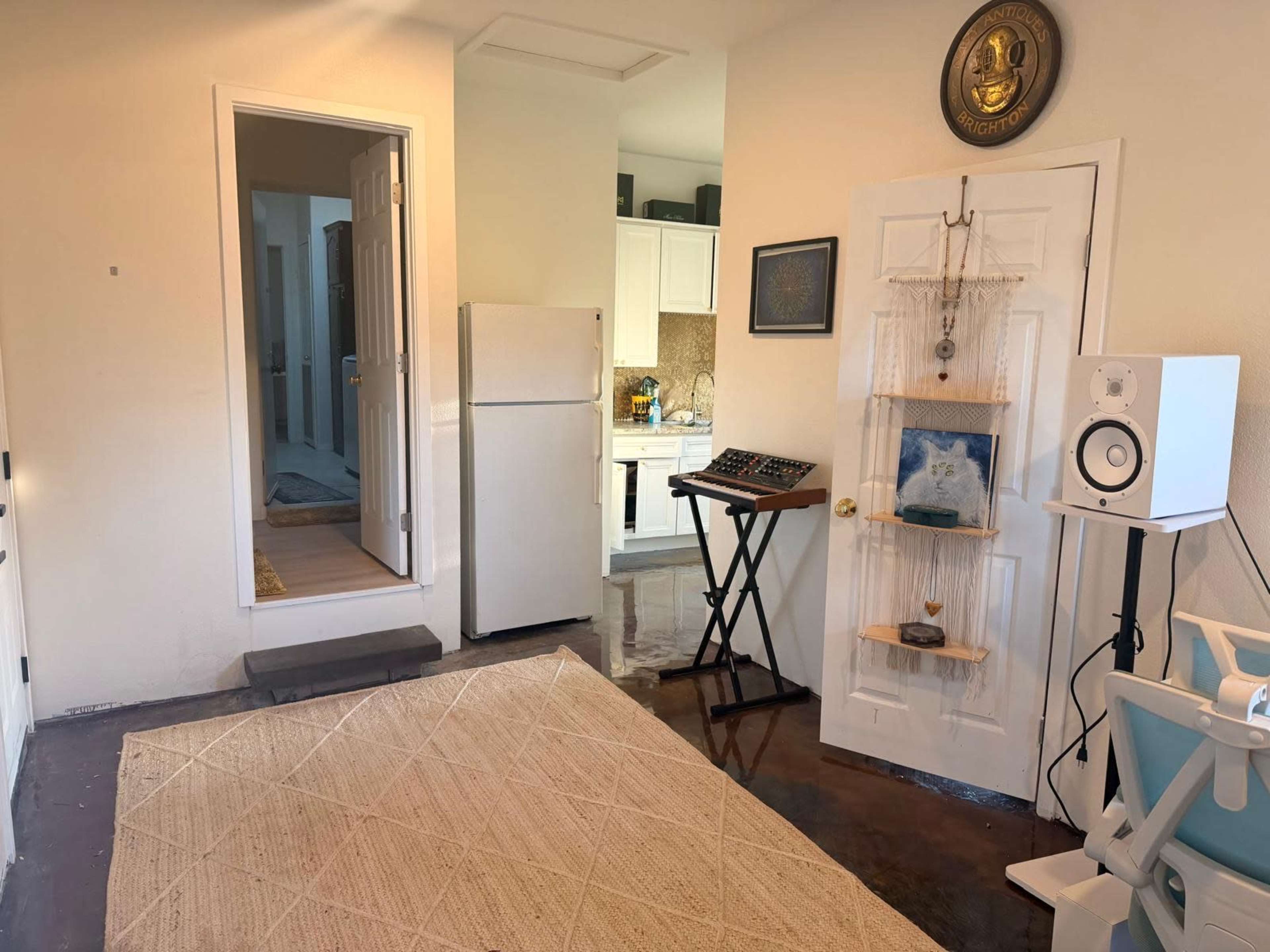 The image shows a small entryway featuring a refrigerator, a kitchen area in the background, a keyboard on a stand, and decorative wall elements.