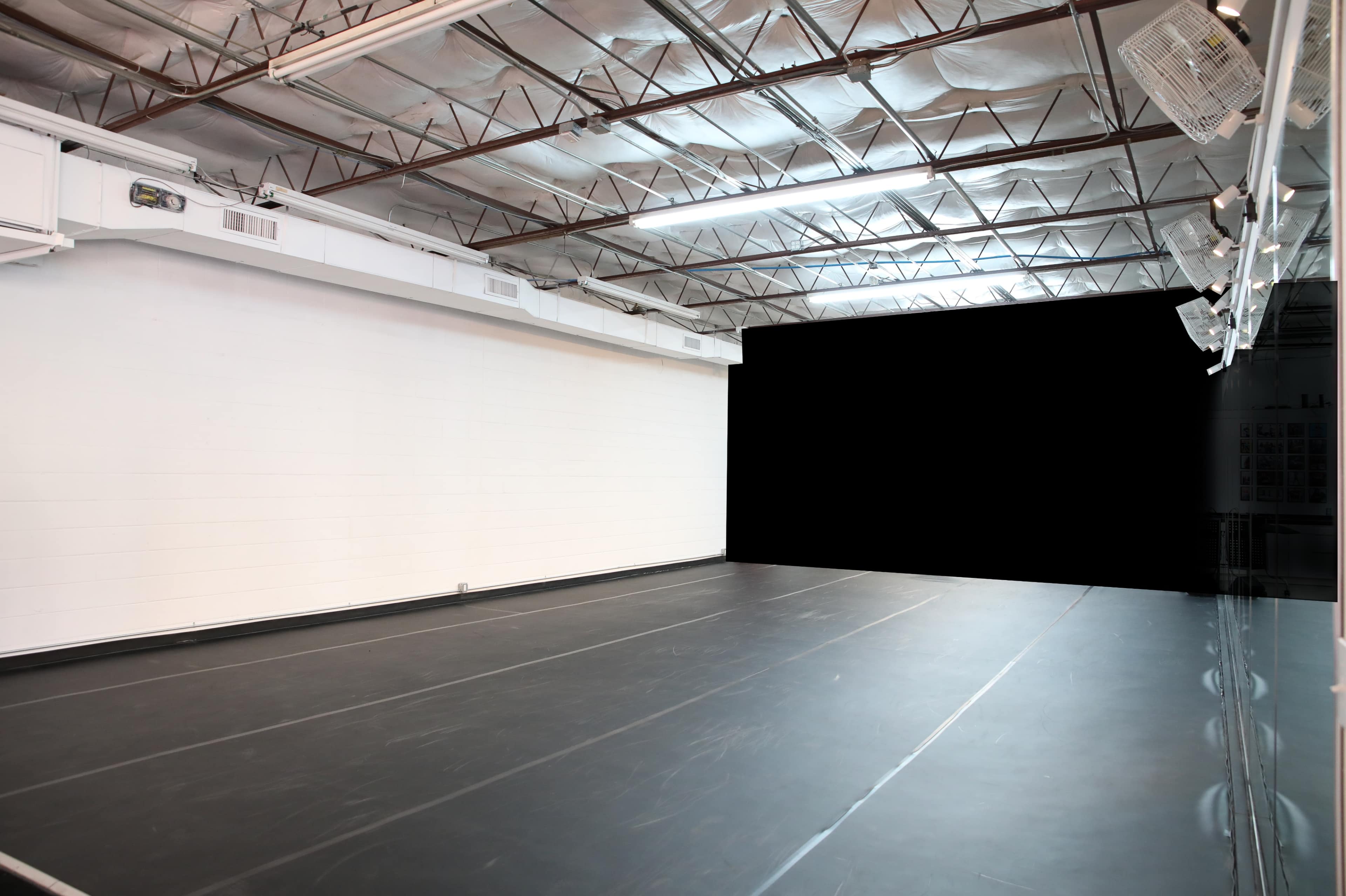 An empty dance studio with a black floor and white walls illuminated by overhead lights.