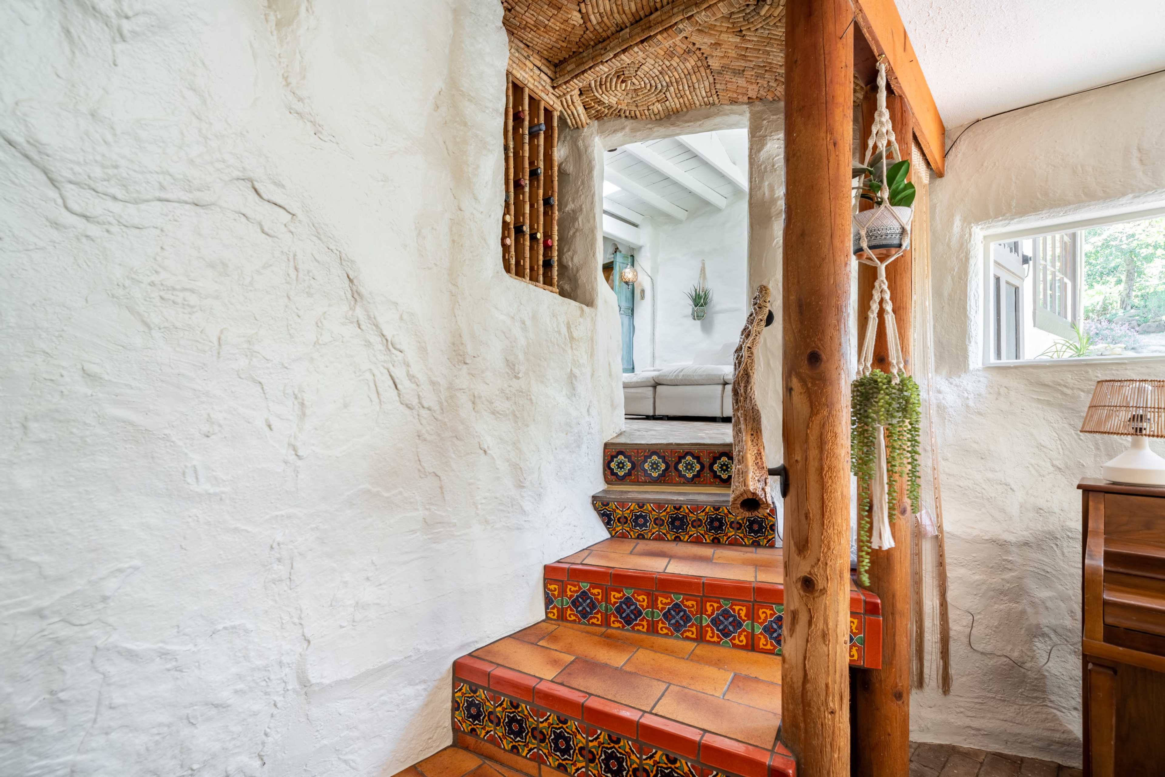 A staircase with colorful tiled steps leads up to a bright, open living area with a textured white wall.