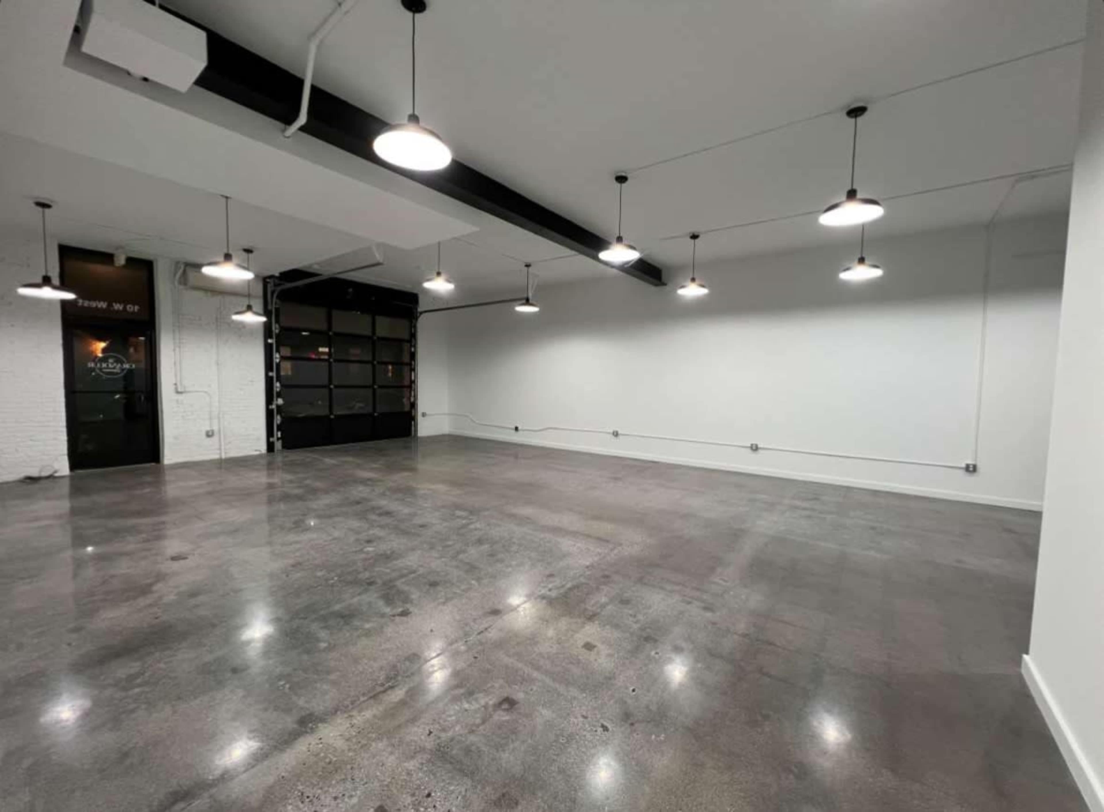 The image shows a large, empty room with a polished concrete floor, white walls, and several hanging lights.