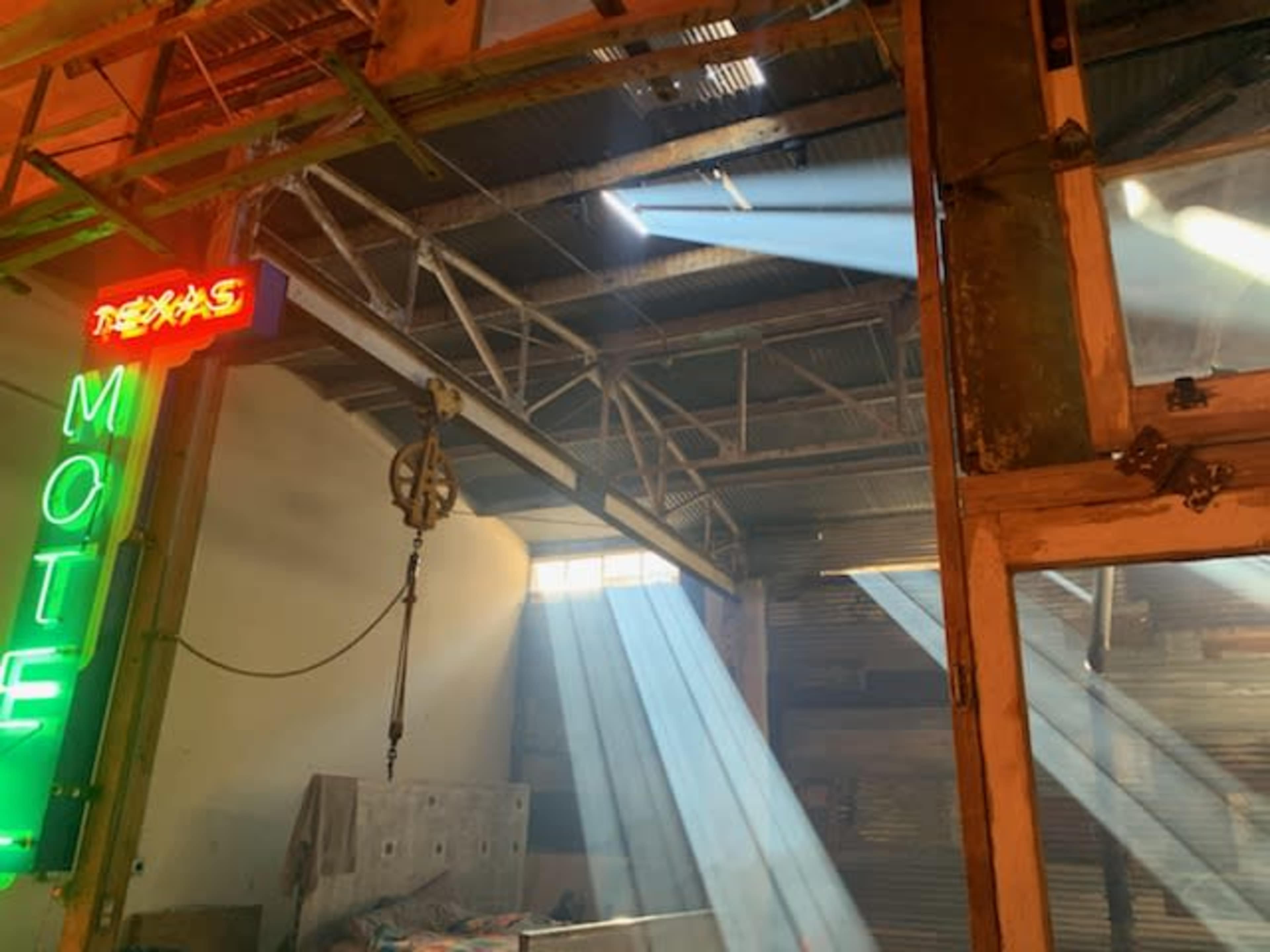 Light beams filter through a window in a rustic, industrial space featuring a neon motel sign.