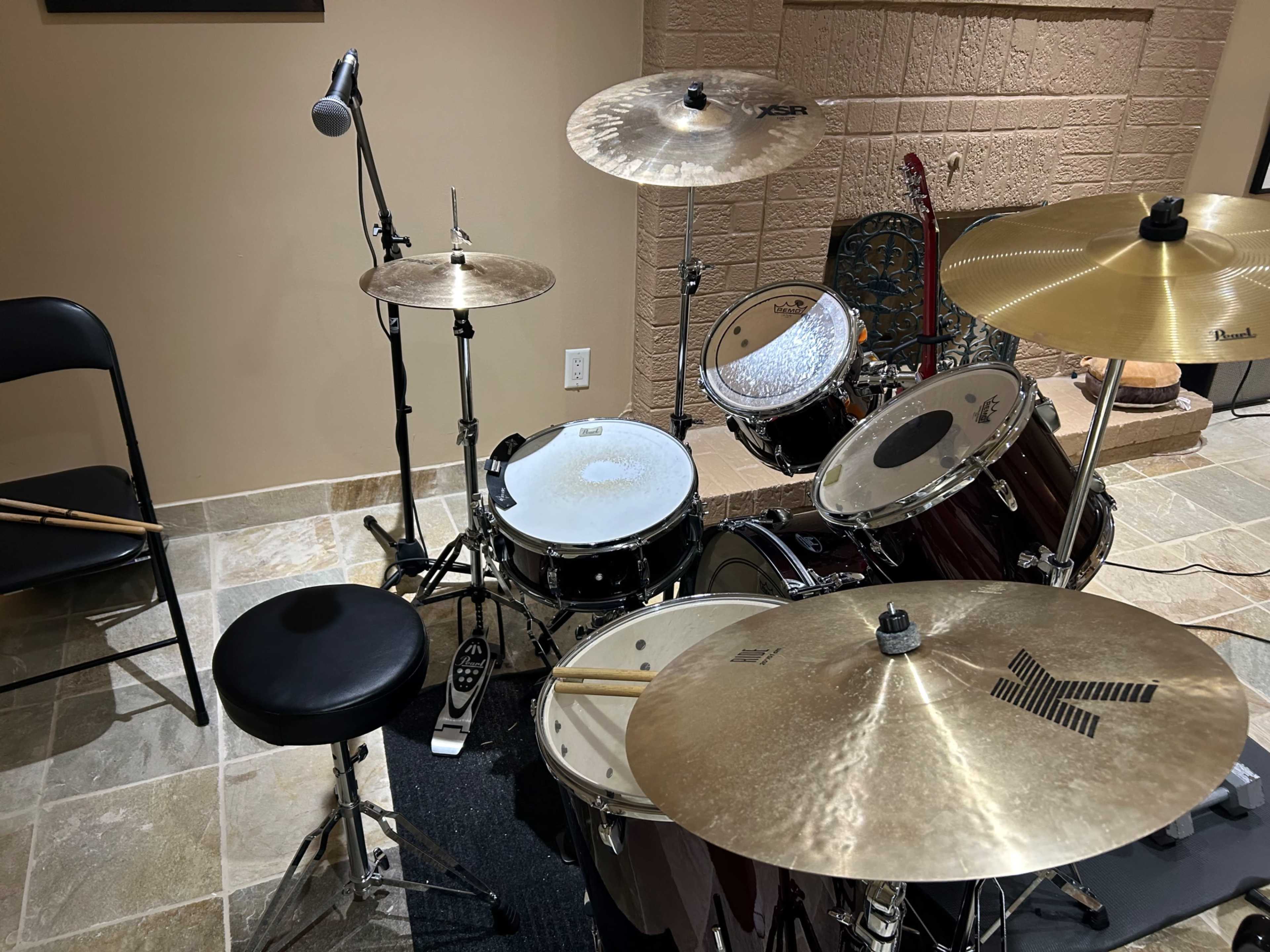 A drum kit set up in a room with a microphone, a stool, and a black chair nearby.