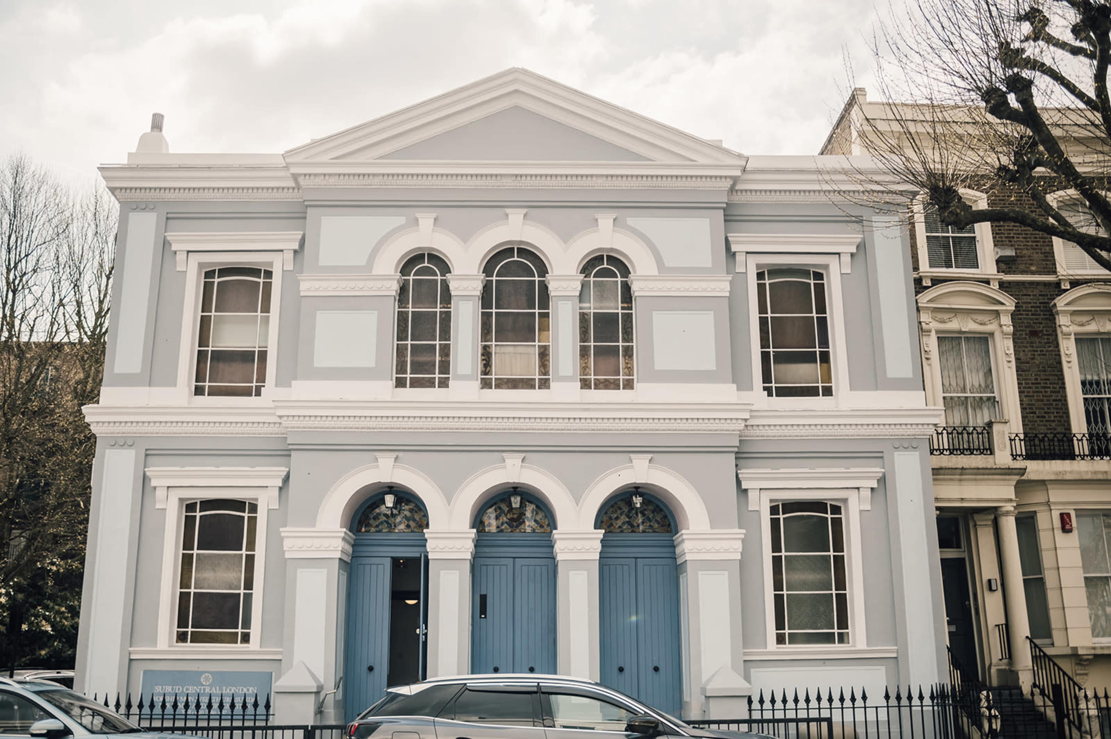 A light blue building with arched windows and two blue doors in a residential area.