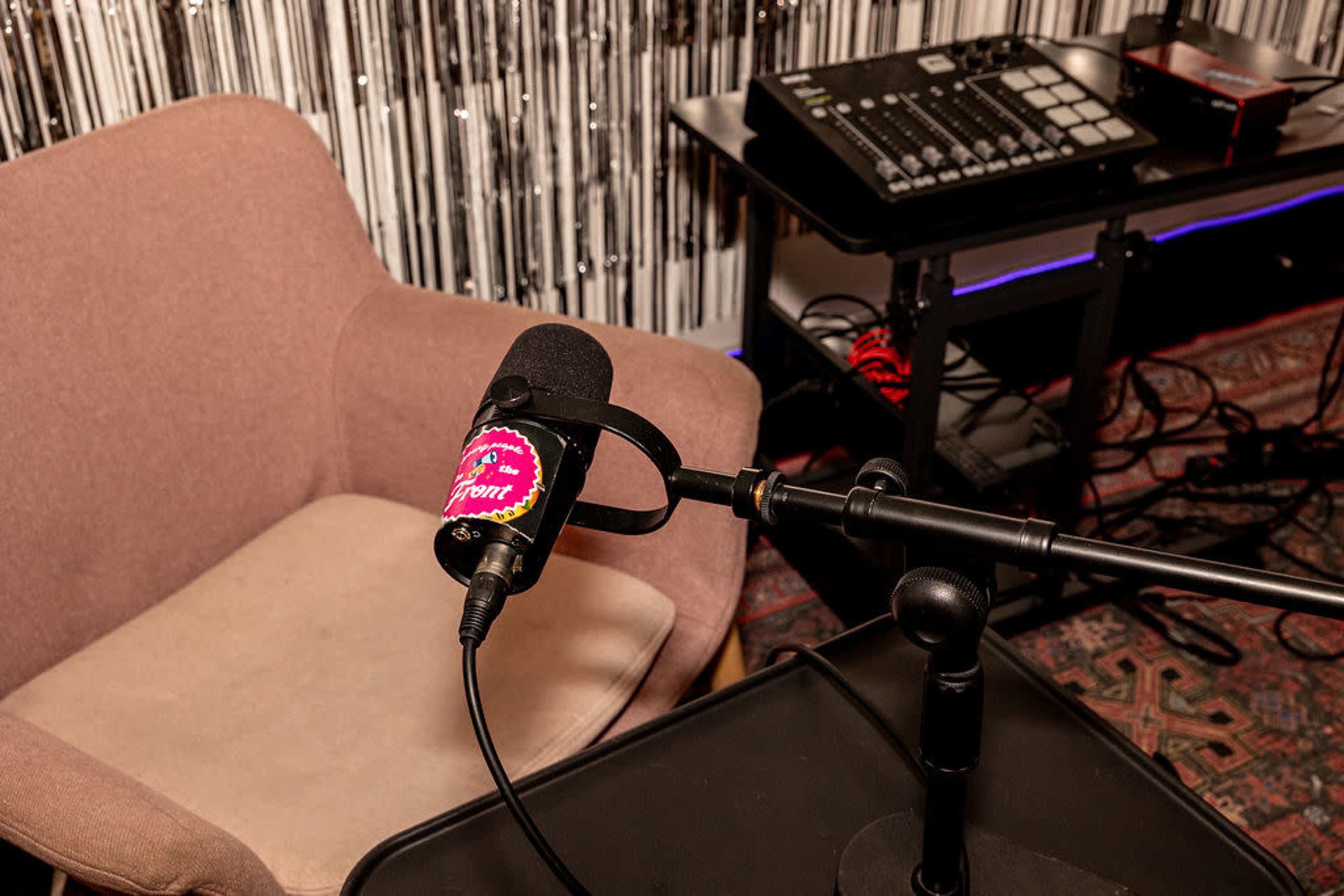 A microphone is positioned on a stand next to a pink chair, with music production equipment visible in the background.