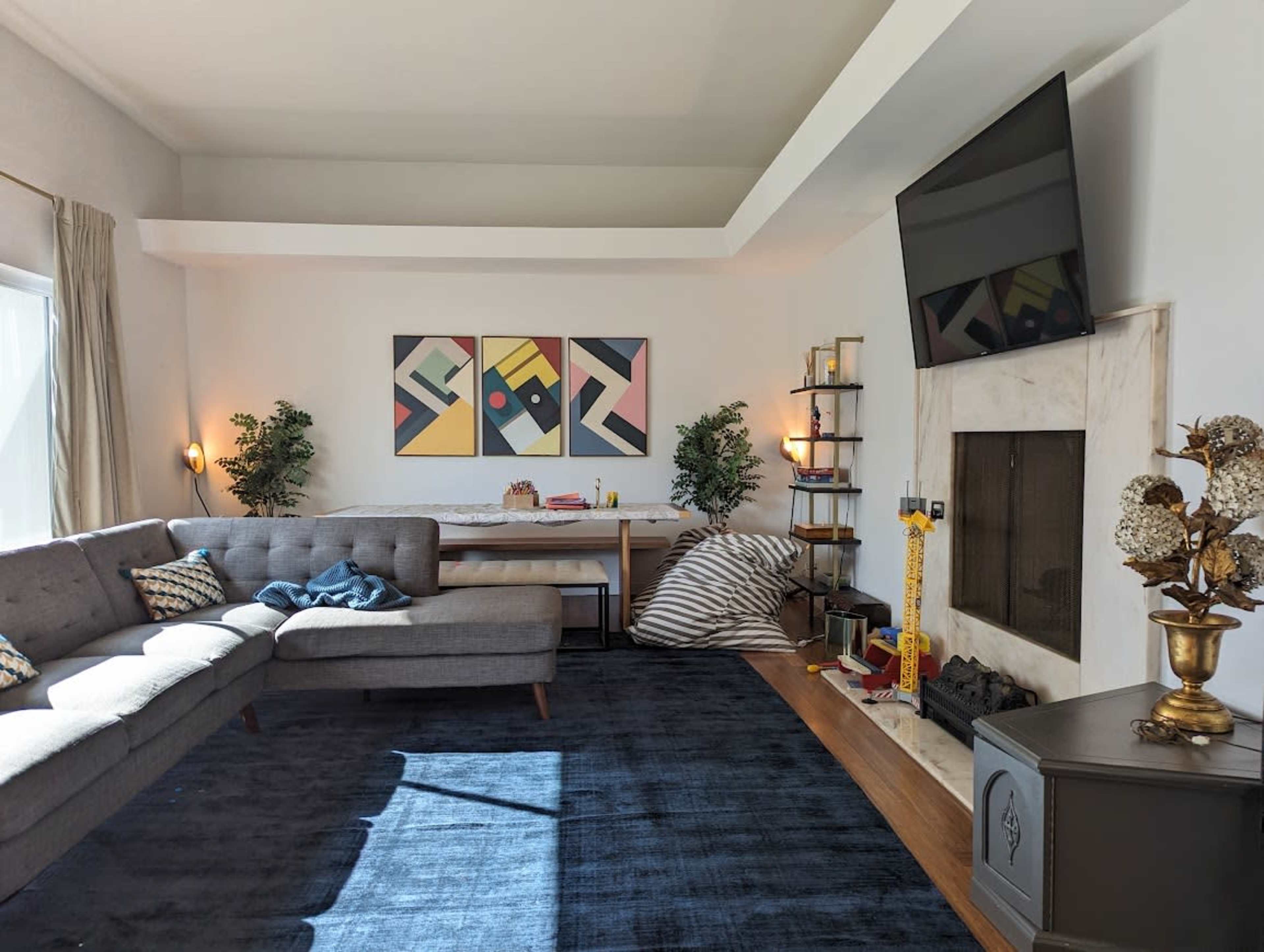 A modern living room features a grey sectional sofa, a large painting on the wall, and a fireplace with decorative items beside it.